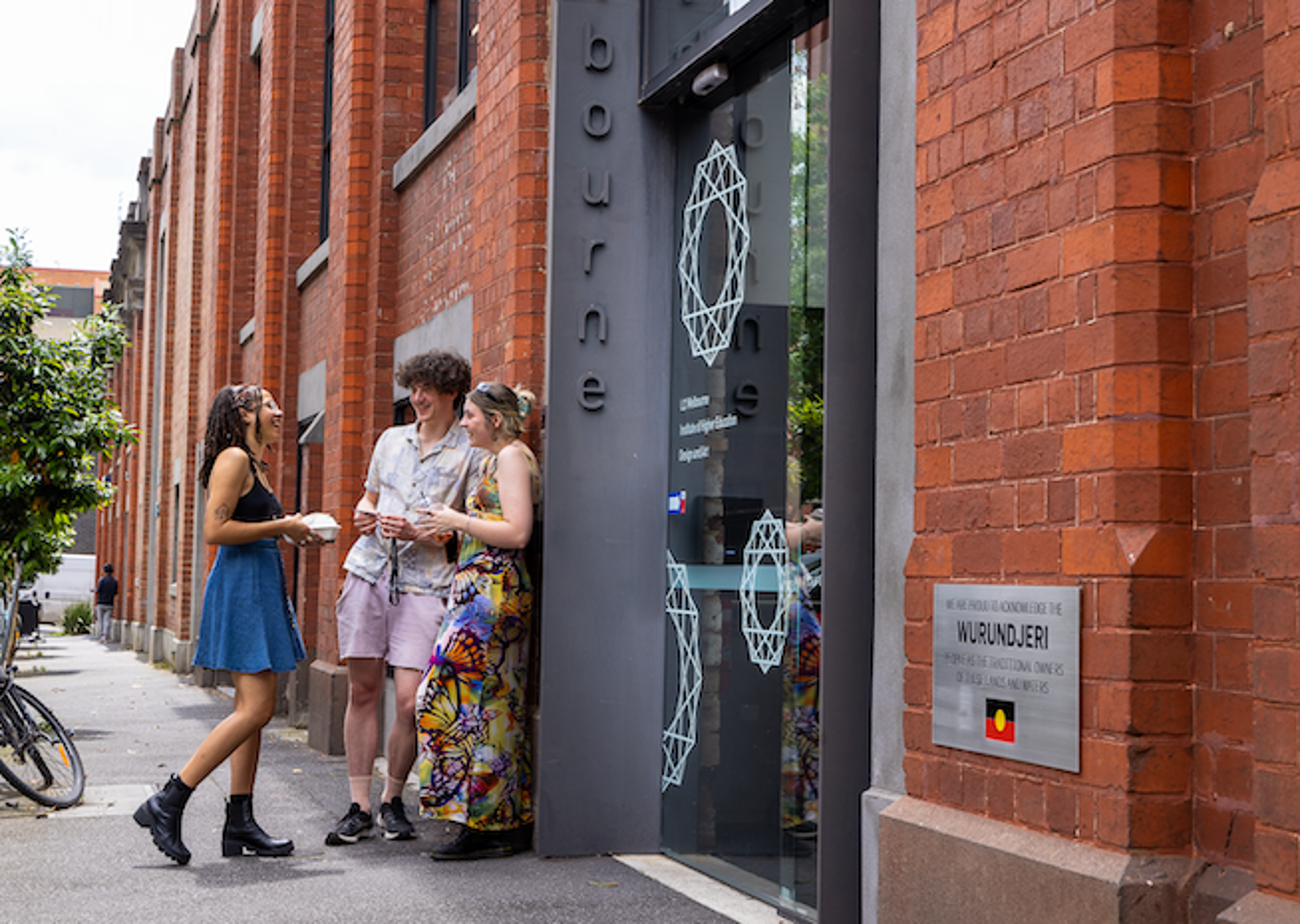 Three friends casually meeting up outside a modern urban building, exchanging smiles and conversation.