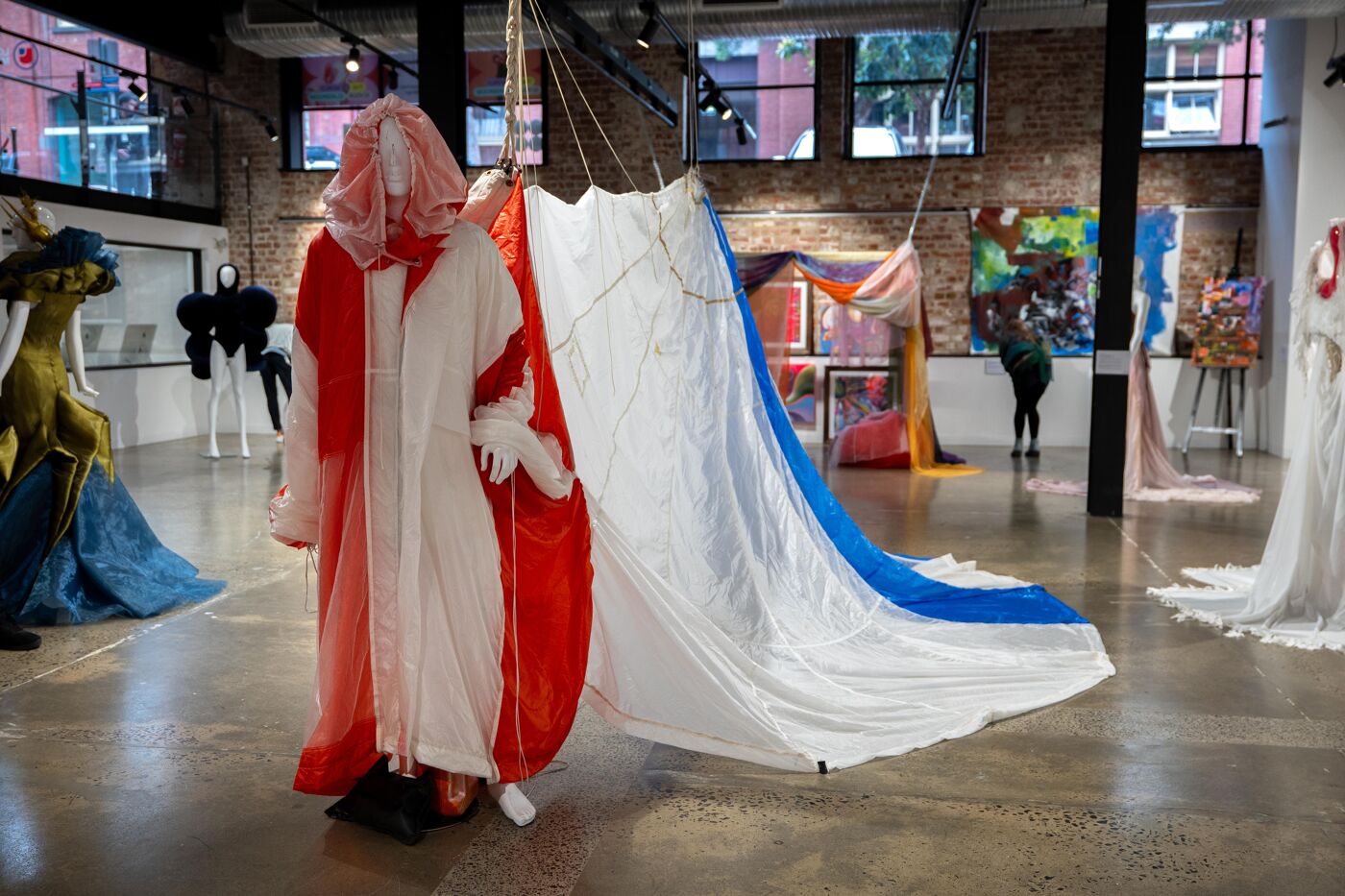 An art exhibition featuring white and red robe-like garments, with a large piece of white and blue fabric spread on the floor.