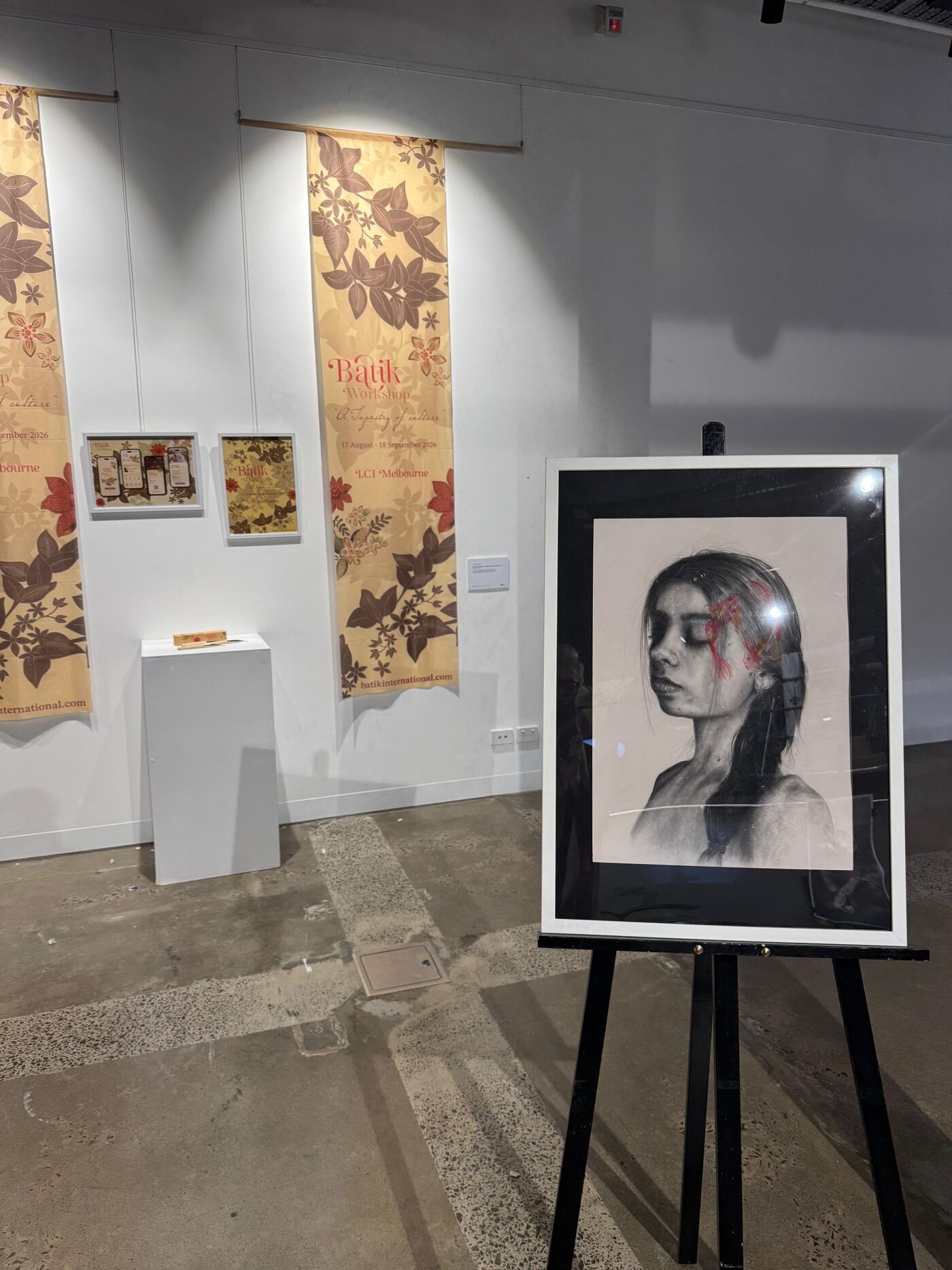 This is an image of an art gallery featuring a framed portrait of a young girl, alongside other artworks displayed on the wall.
