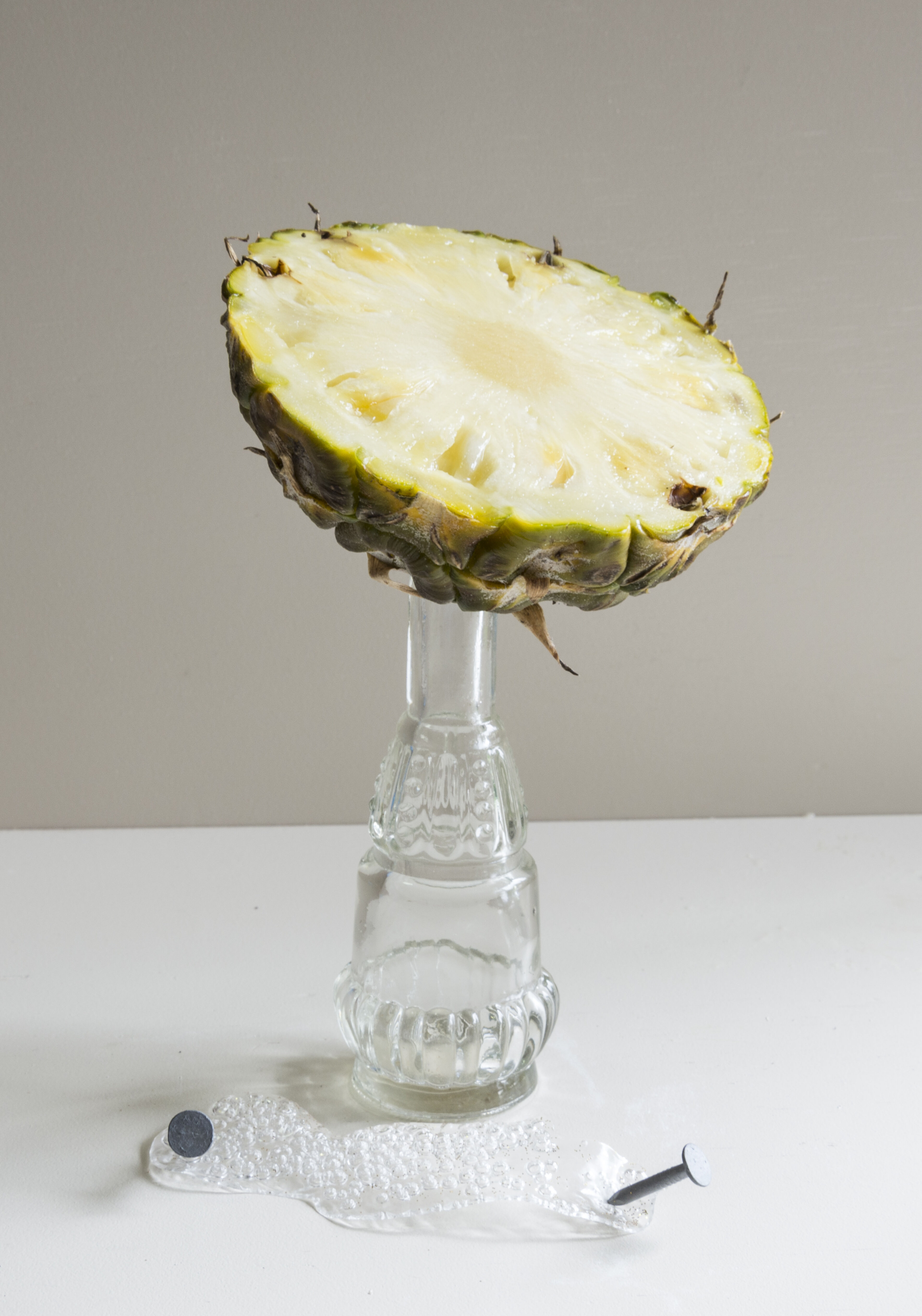 A halved pineapple presented upside-down on a clear glass pedestal, with artistic flair.