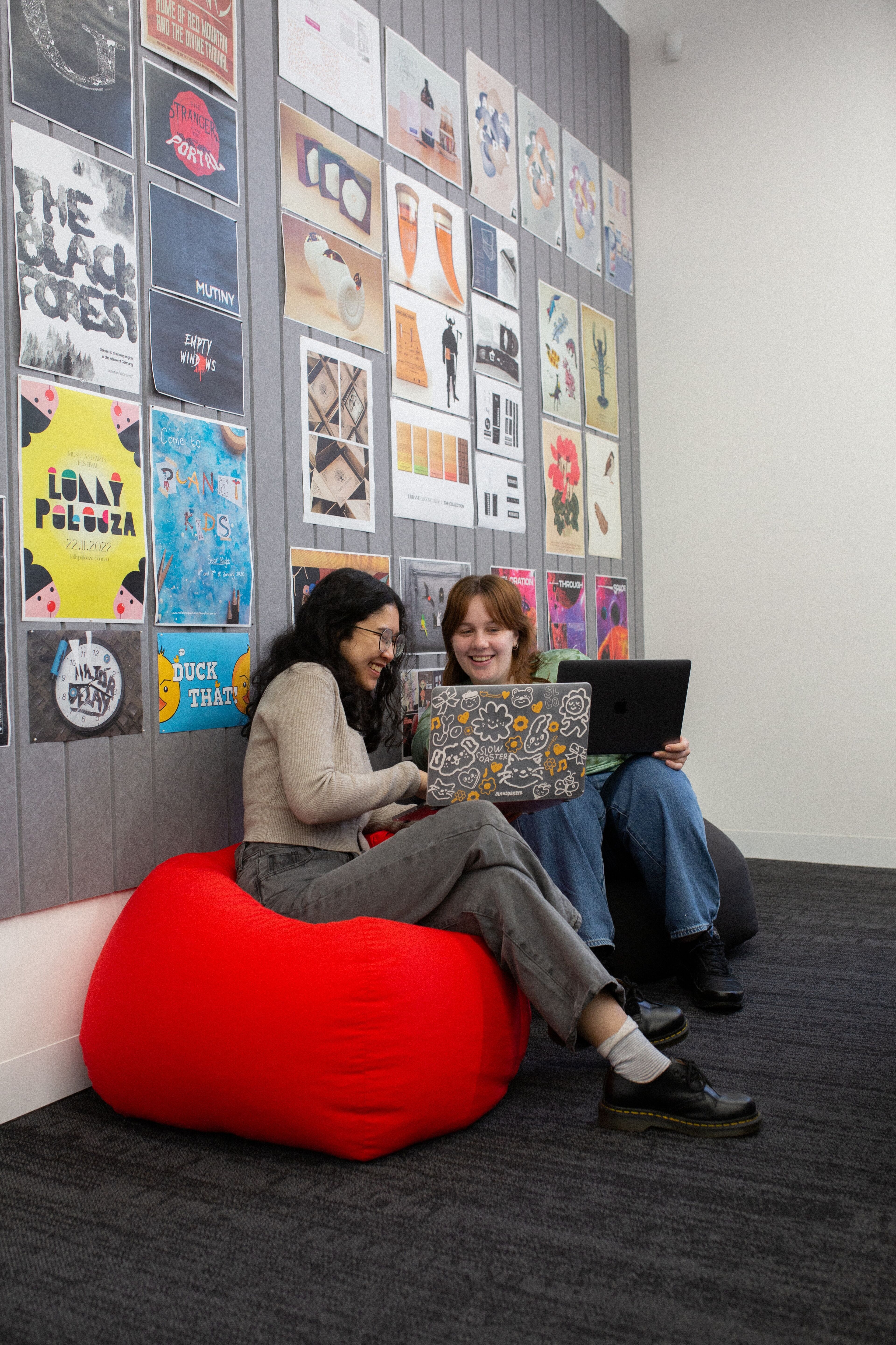 Deux étudiantes rient et partagent des idées sur un pouf rouge dans un salon étudiant dynamique.