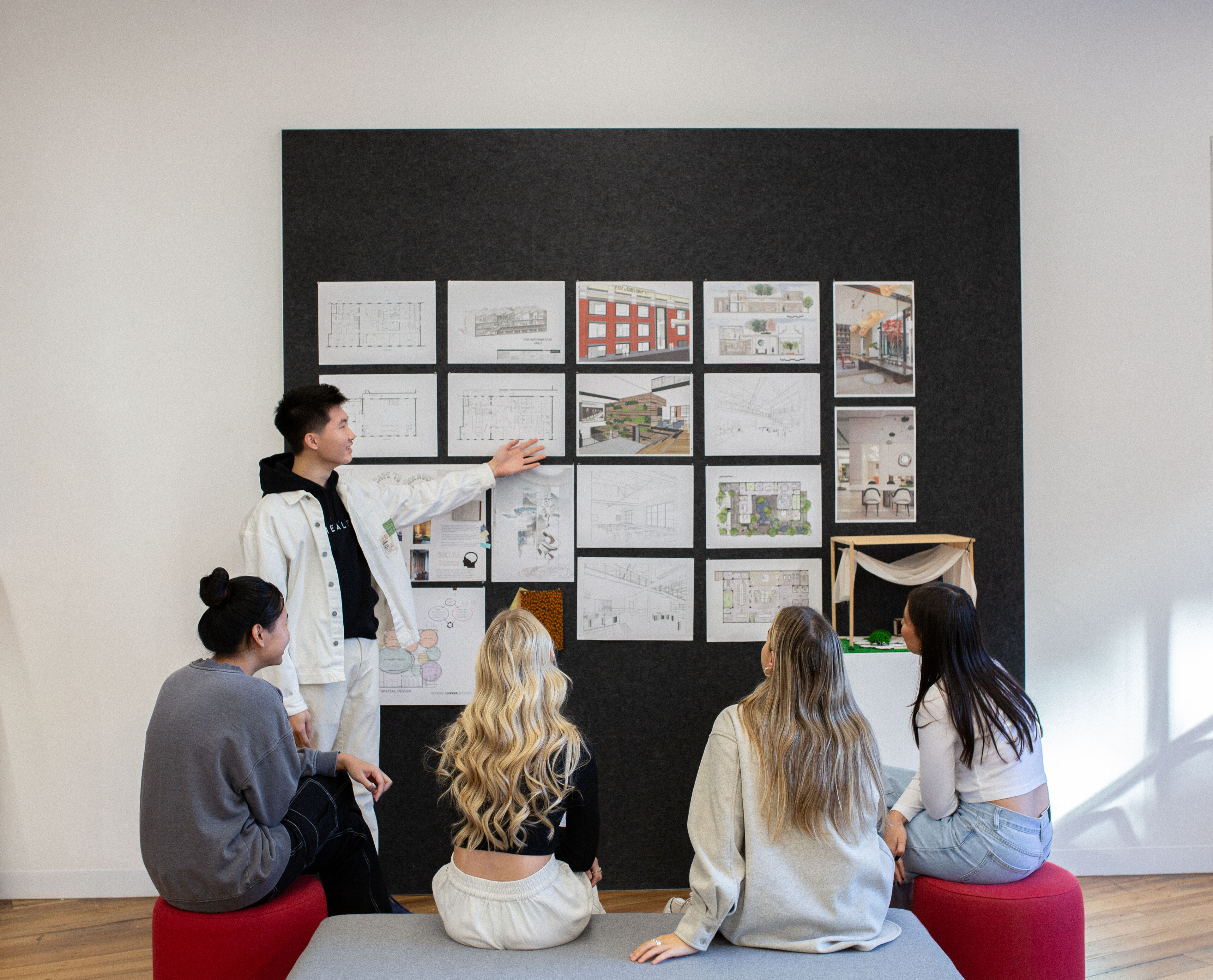 A student presenting interior design to a group of attentive peers in a modern classroom.