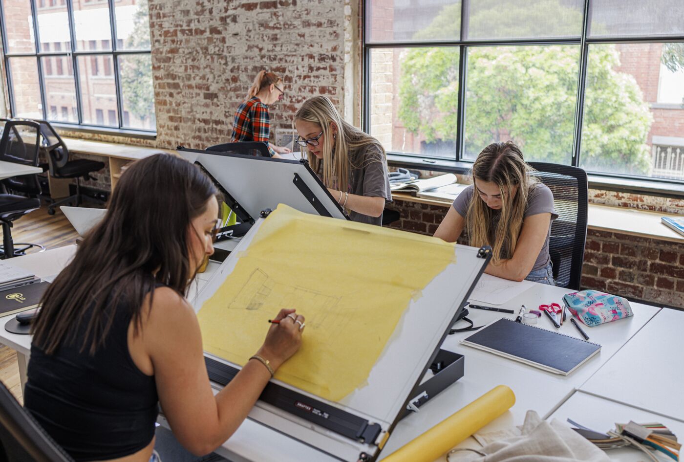 A group of focused designers collaborate over architectural blueprints in a sunlit, urban studio setting.