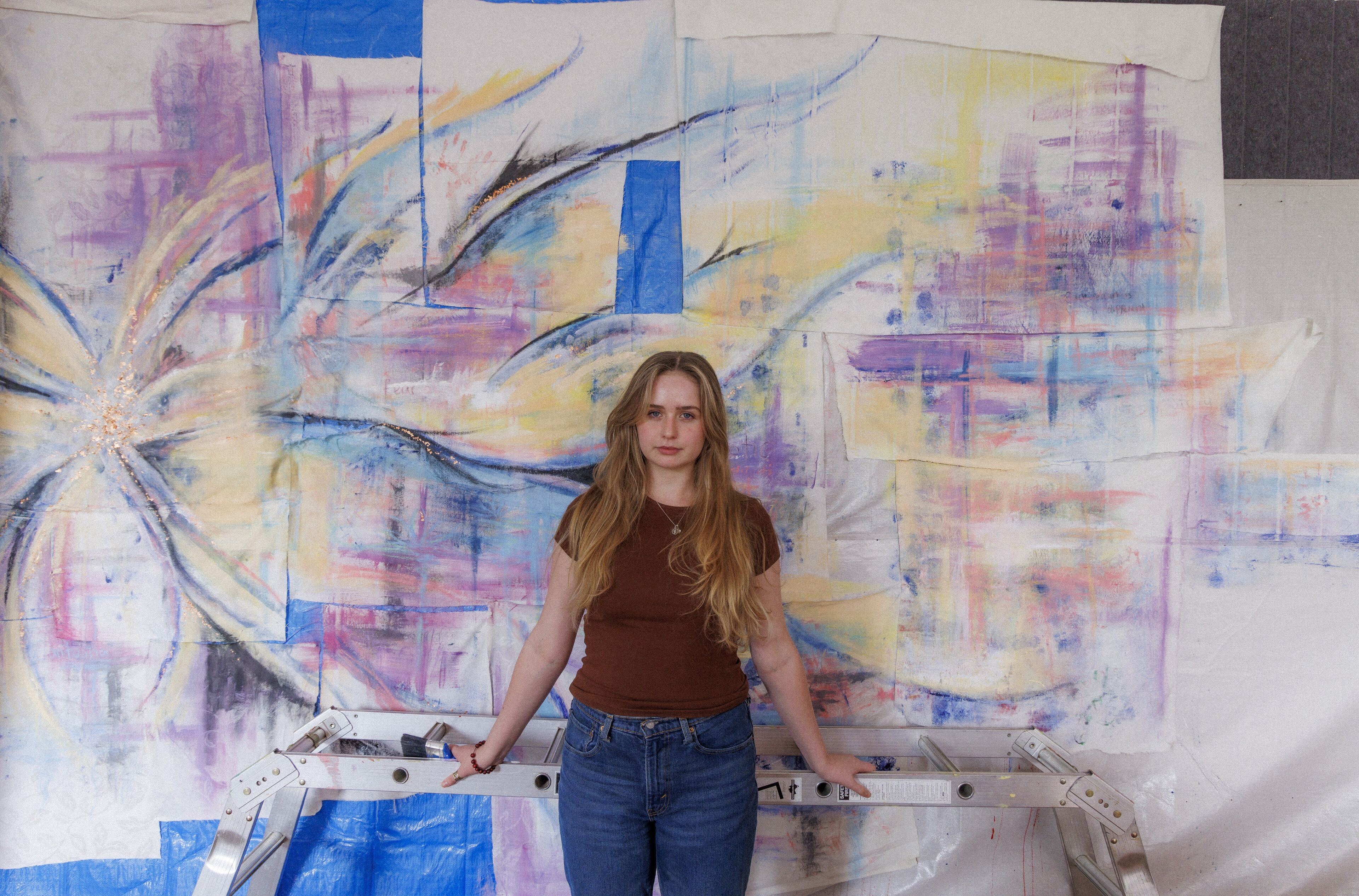 An artist stands resolute before her expressive, abstract painting on a large canvas.