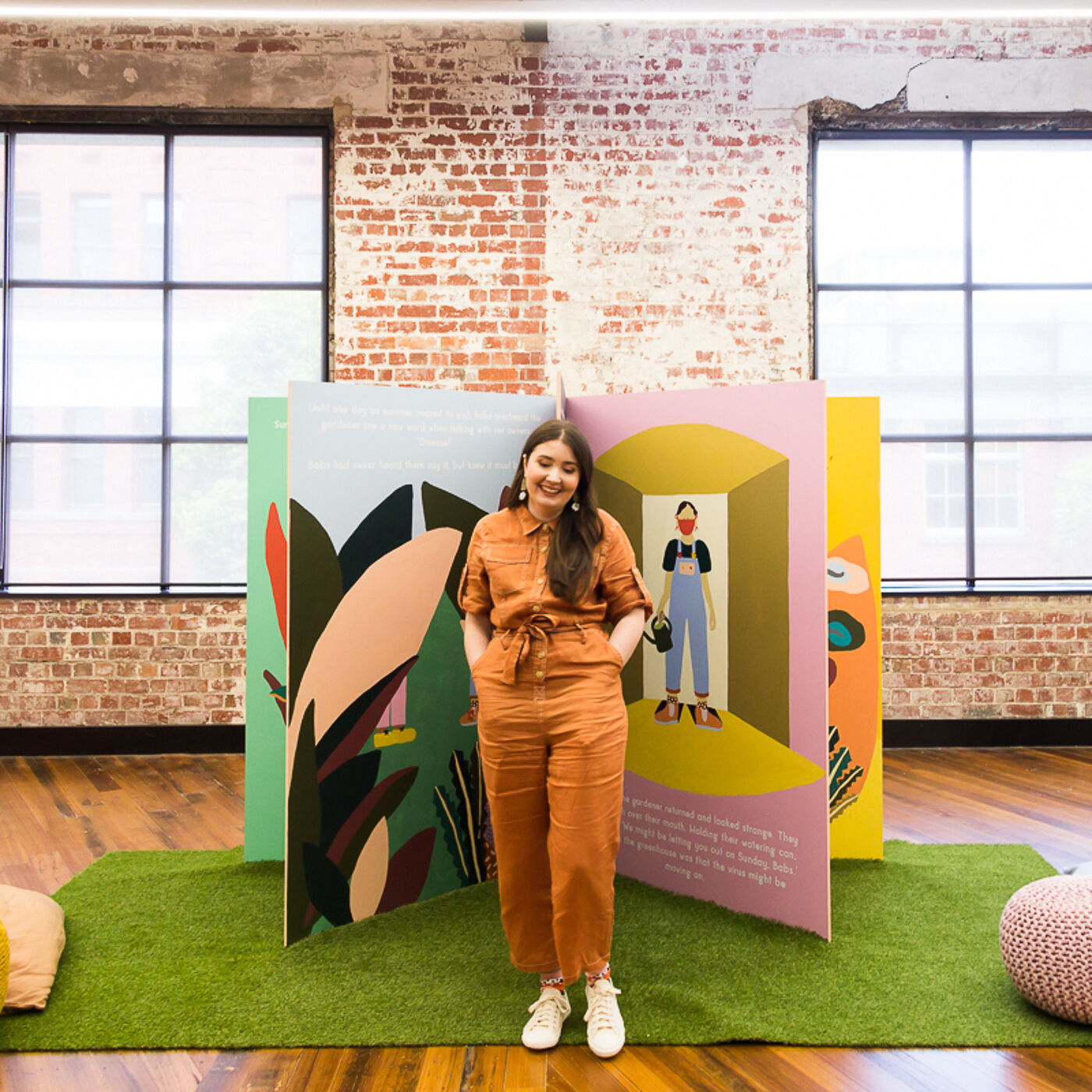 A student smiling beside a vibrant art display at a college exhibition.