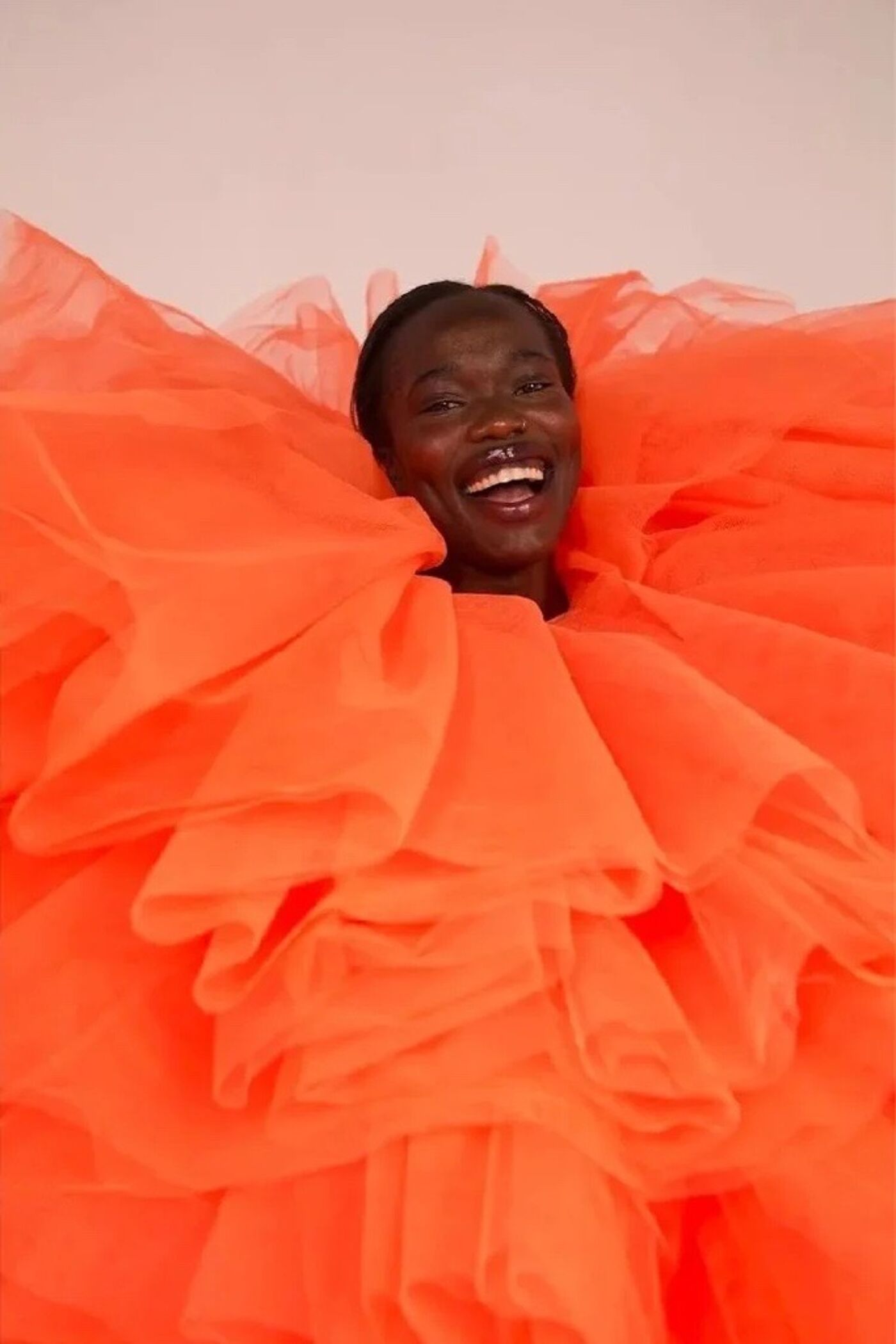 The image showcases a person joyfully smiling, their face framed by a vibrant orange, ruffled garment. The bright color and texture create a visually striking and cheerful composition.