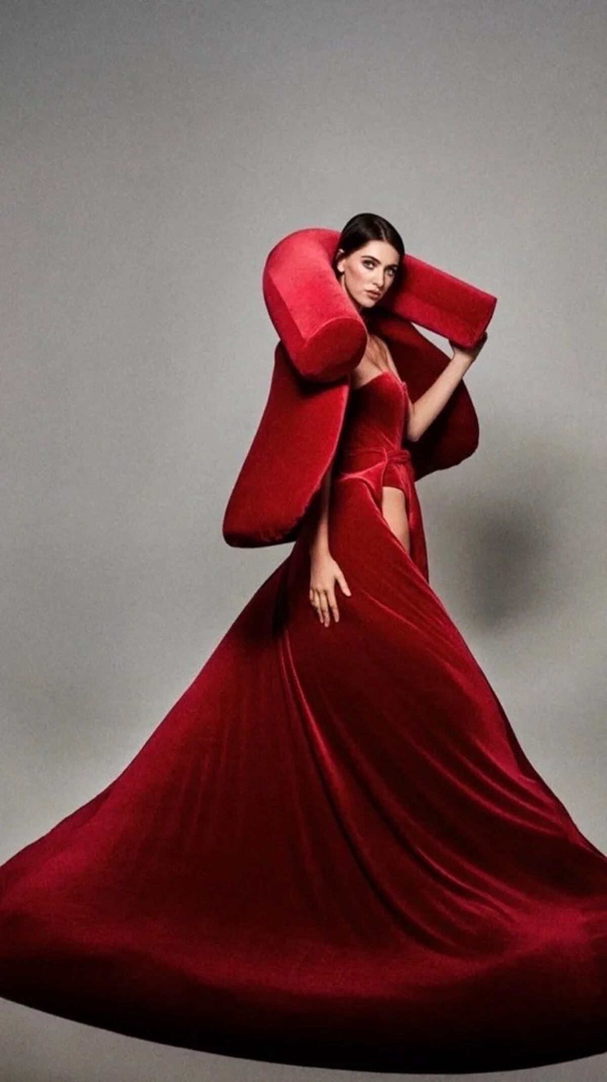 The image showcases a woman in a stunning red velvet gown with a dramatic, oversized collar. The dress has a flowing train, creating a bold and elegant fashion statement.