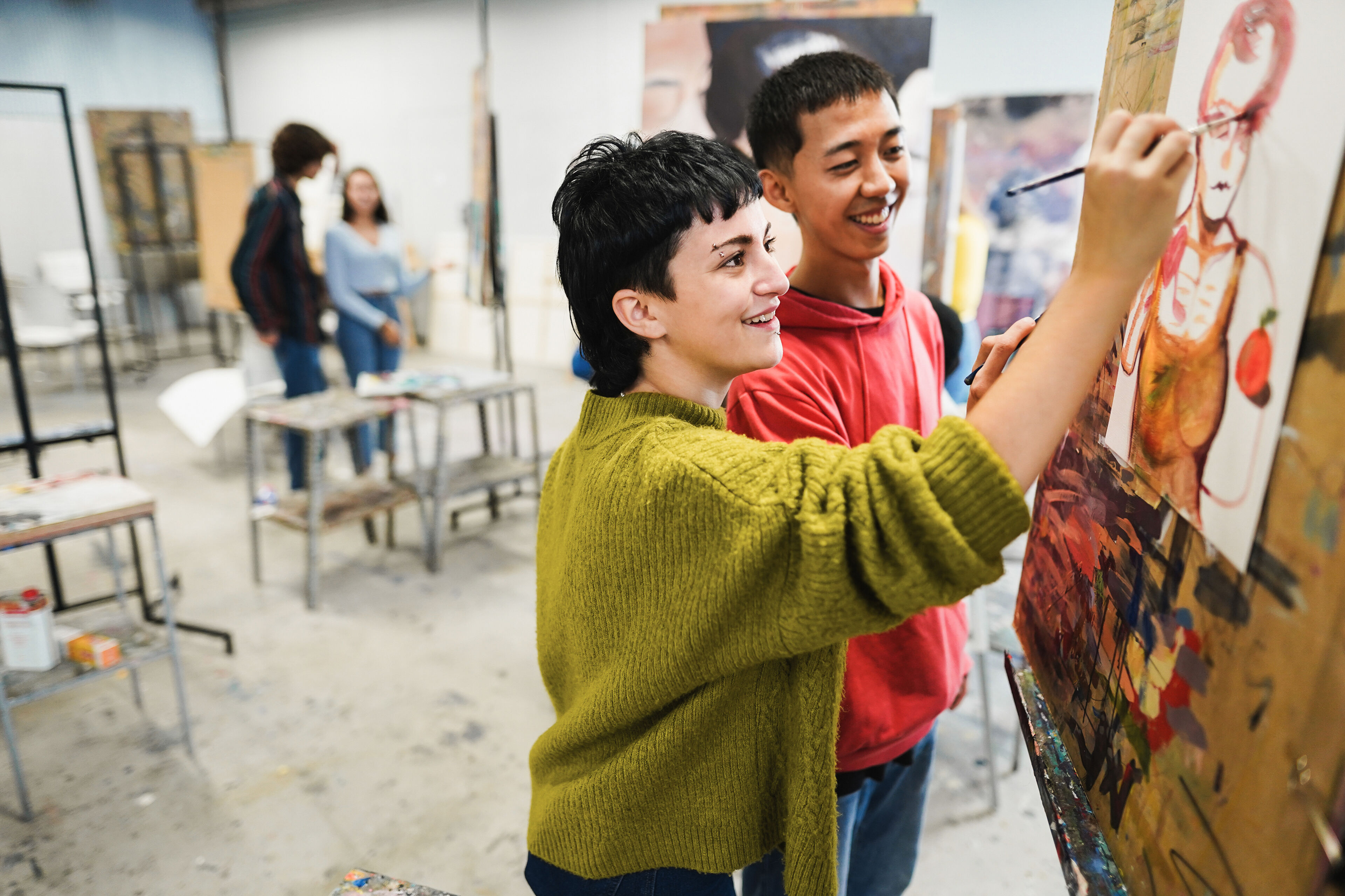 Two joyful students collaborate on a vibrant painting in an art studio.