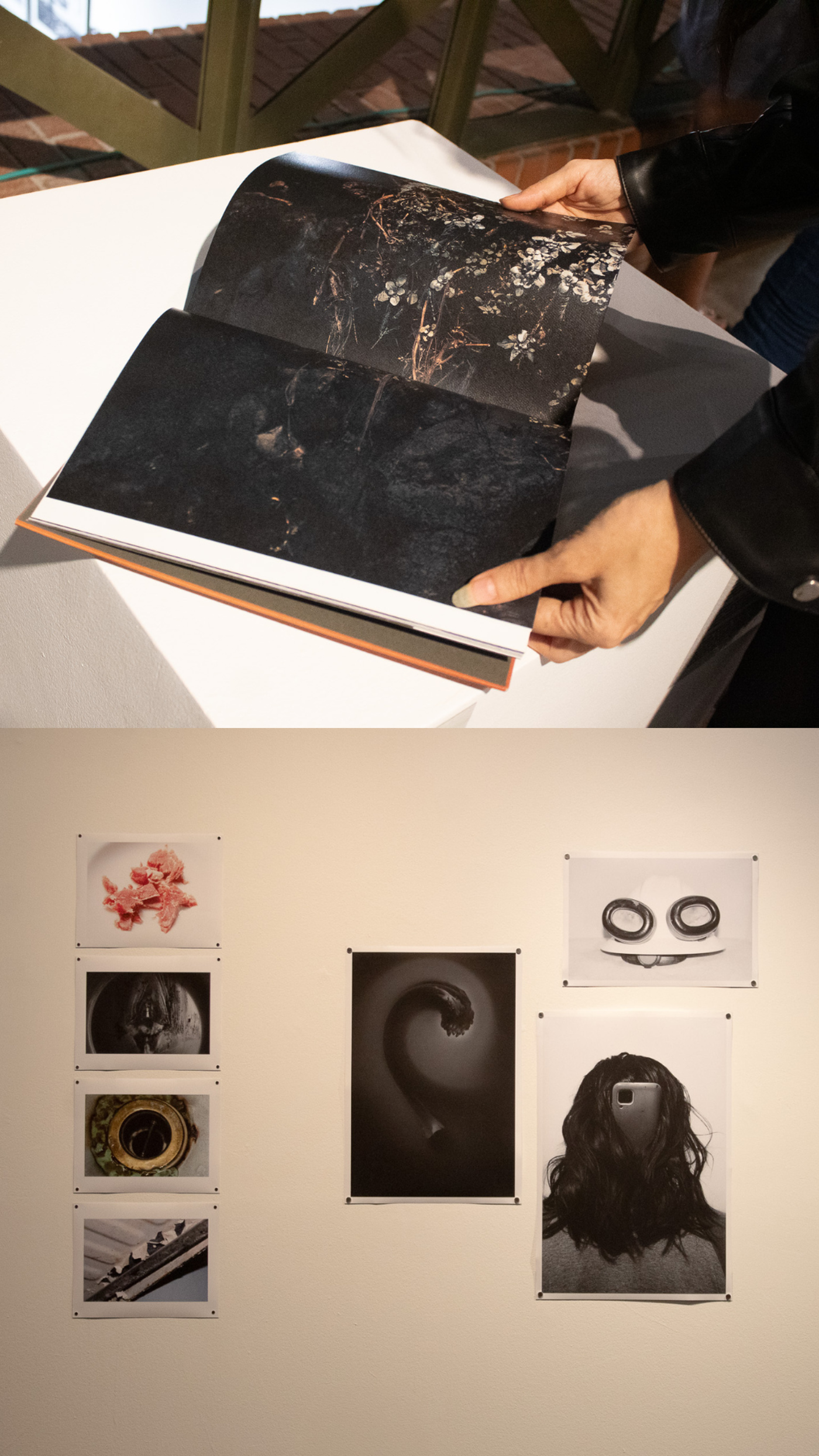 The image shows a person holding a book with dark, abstract imagery. Below, a collection of black and white photographs are displayed on a white wall, creating an art exhibition-like setting.