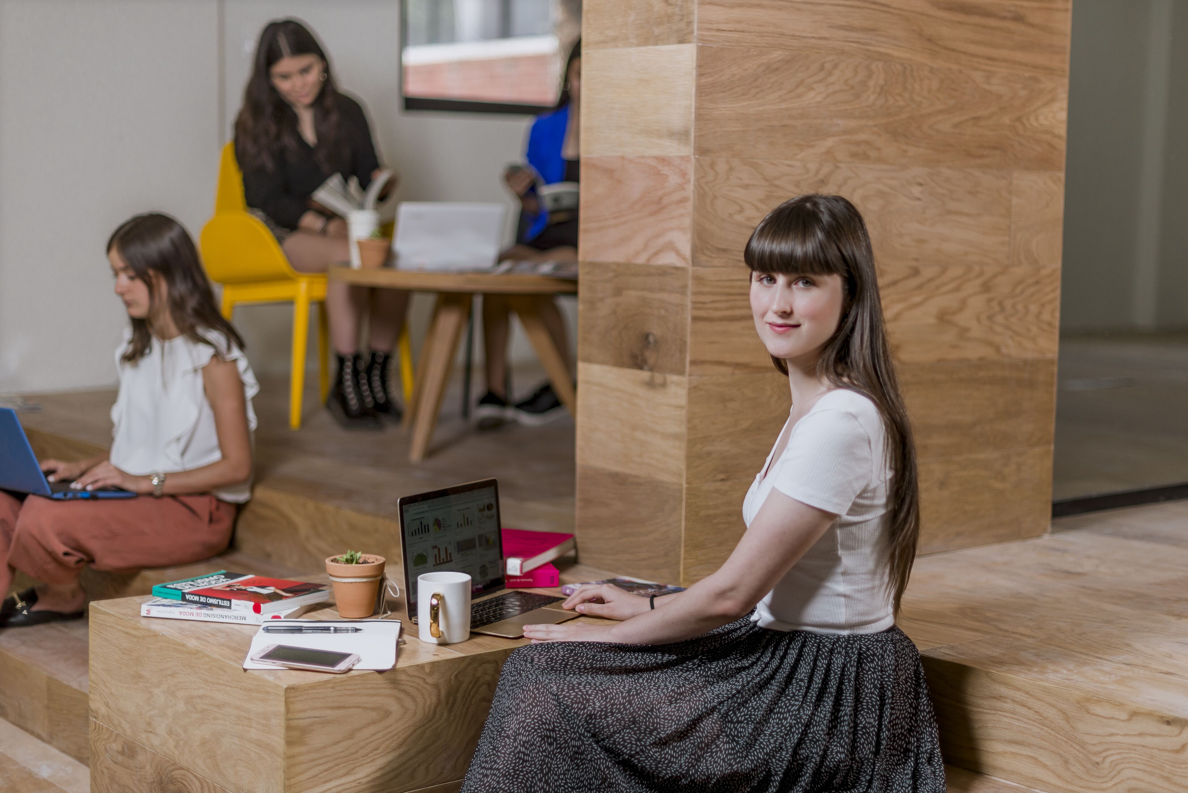 A student with a laptop and books sits poised for learning in a modern, collaborative space.