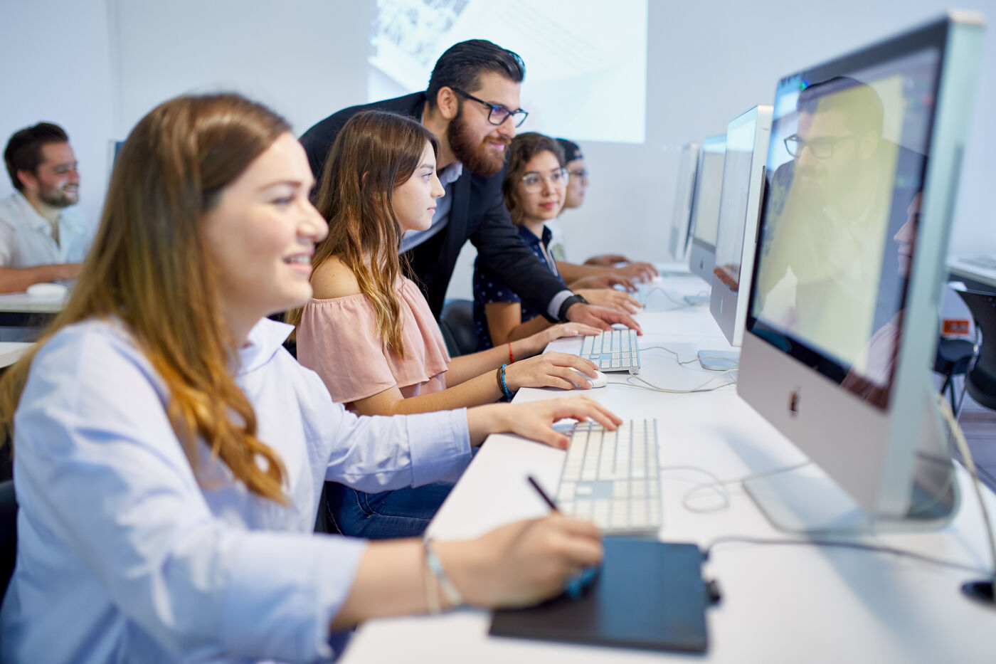 Students and a teacher interact in a computer lab, showcasing a dynamic educational experience.