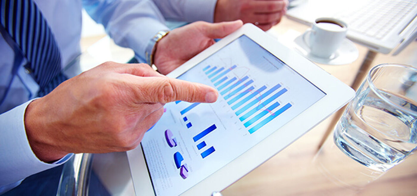 Business professionals analyze financial charts on a digital tablet, focusing on data to guide strategic decisions in a corporate setting.