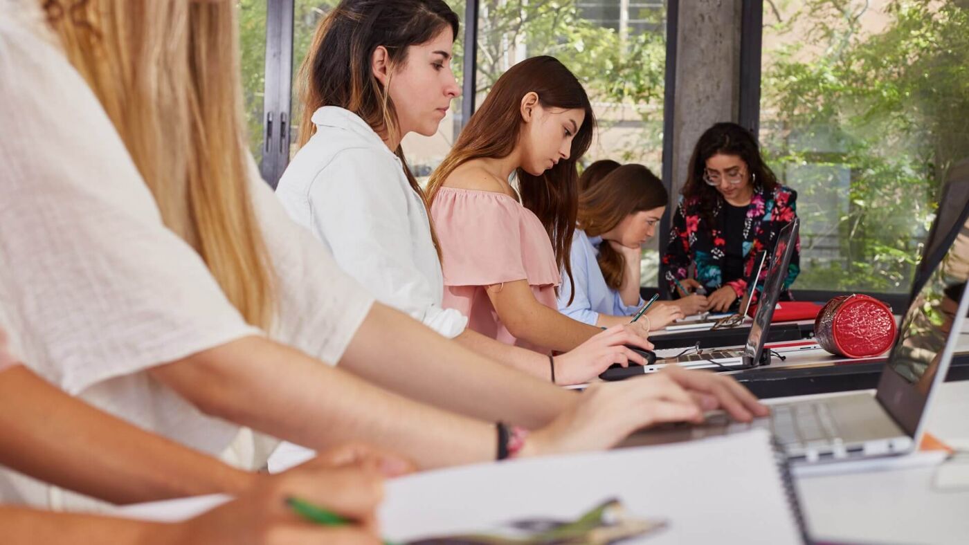 A focused group of female students collaboratively working on their assignments in a well-lit classroom, embodying teamwork and dedication.