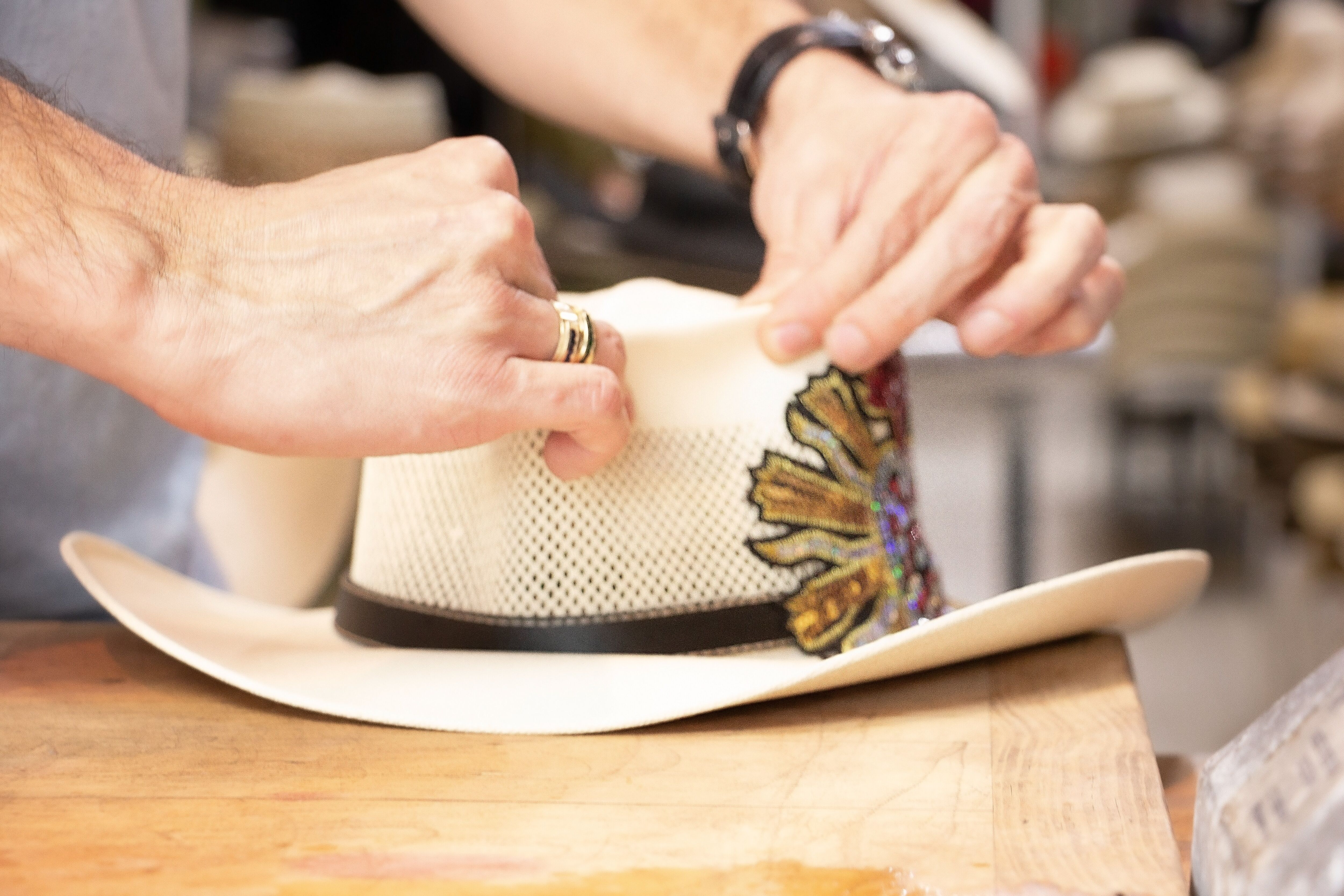 Primer plano de las manos de un artesano añadiendo meticulosamente bordados coloridos a un sombrero de vaquero blanco en un taller.