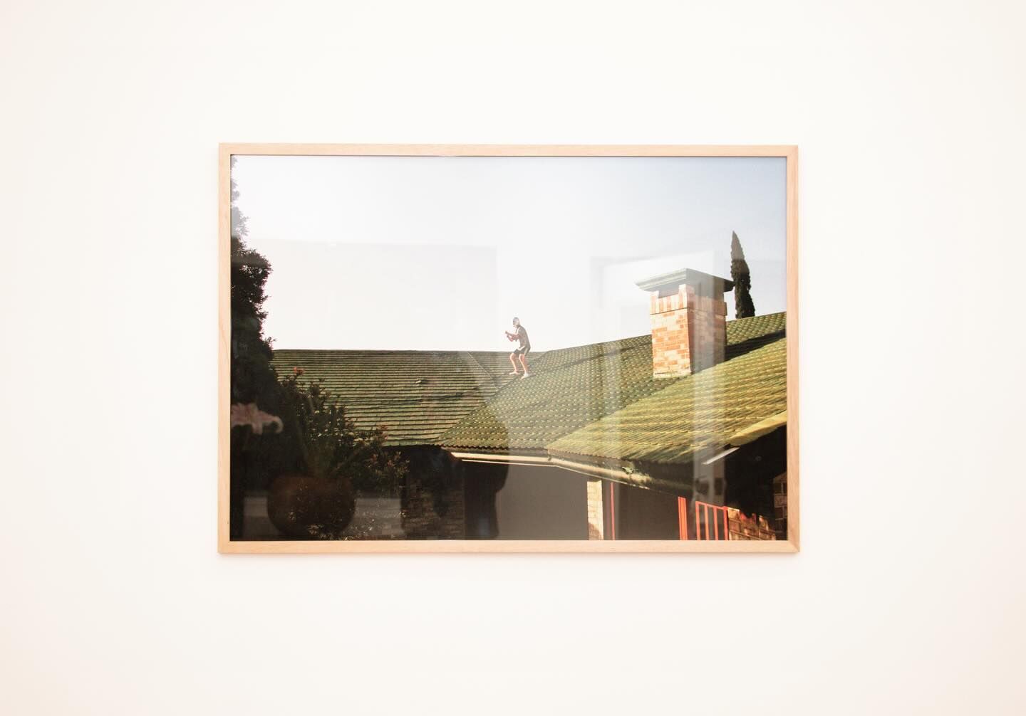 Una fotografía expuesta en una galería de arte que muestra una imagen surrealista de una persona caminando aparentemente sobre un tejado, mezclando la realidad con la imaginación artística.