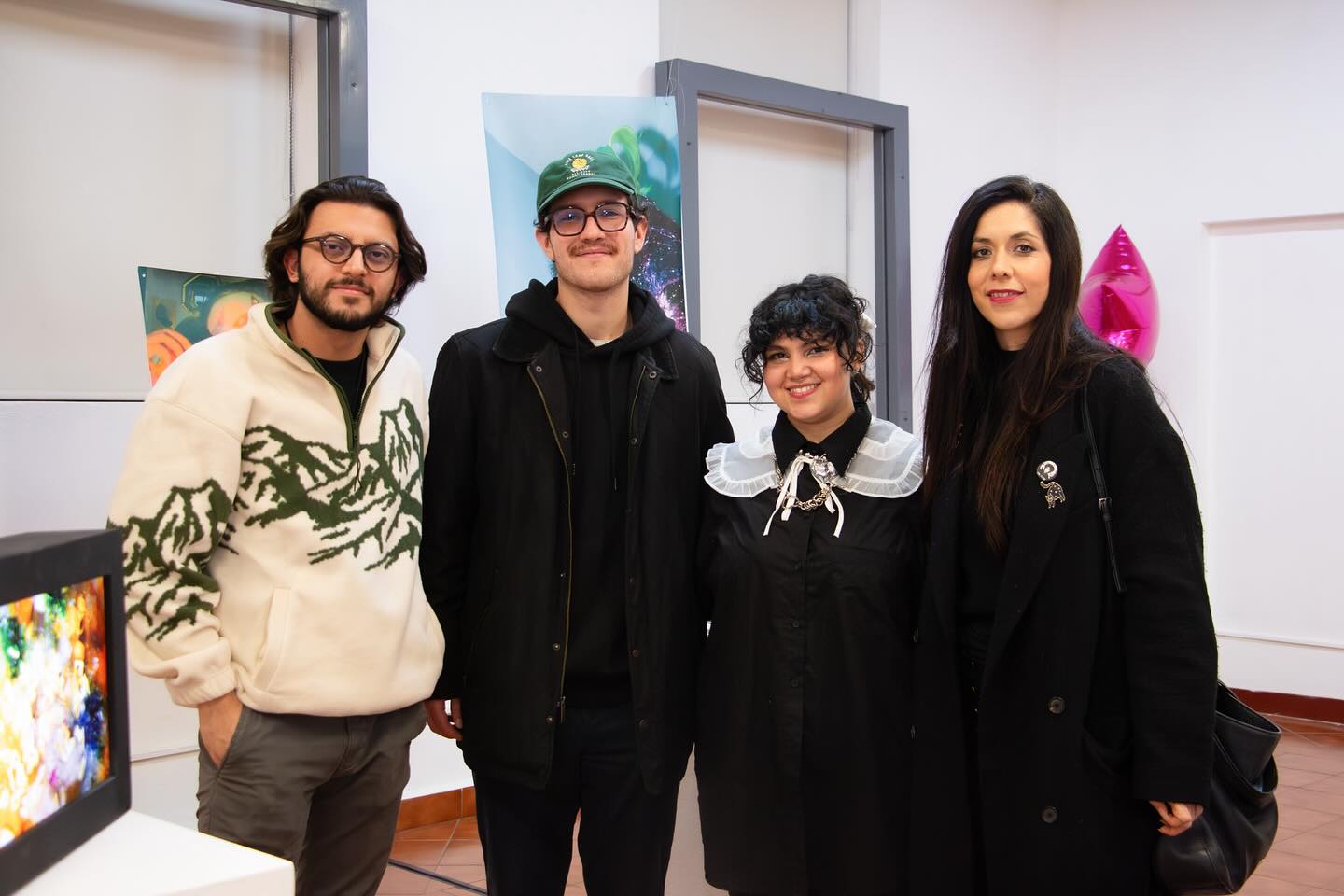 Cuatro entusiastas del arte posan juntos en una exposición, sus estilos personales únicos complementan el ambiente creativo de la galería.