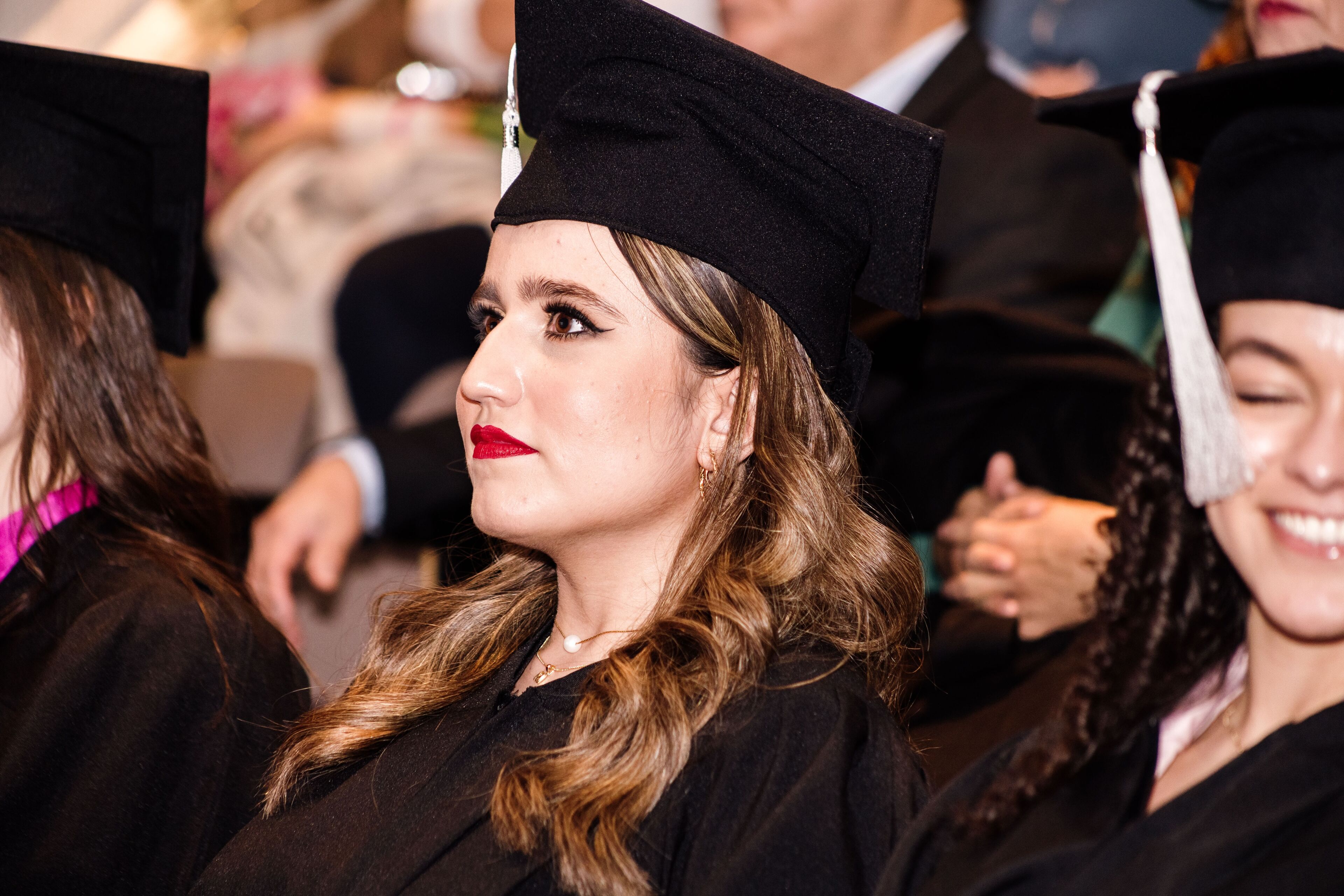 Una graduada en toga y birrete tradicionales, adornada con un maquillaje audaz, refleja una sensación de logro y orgullo durante la ceremonia de graduación.