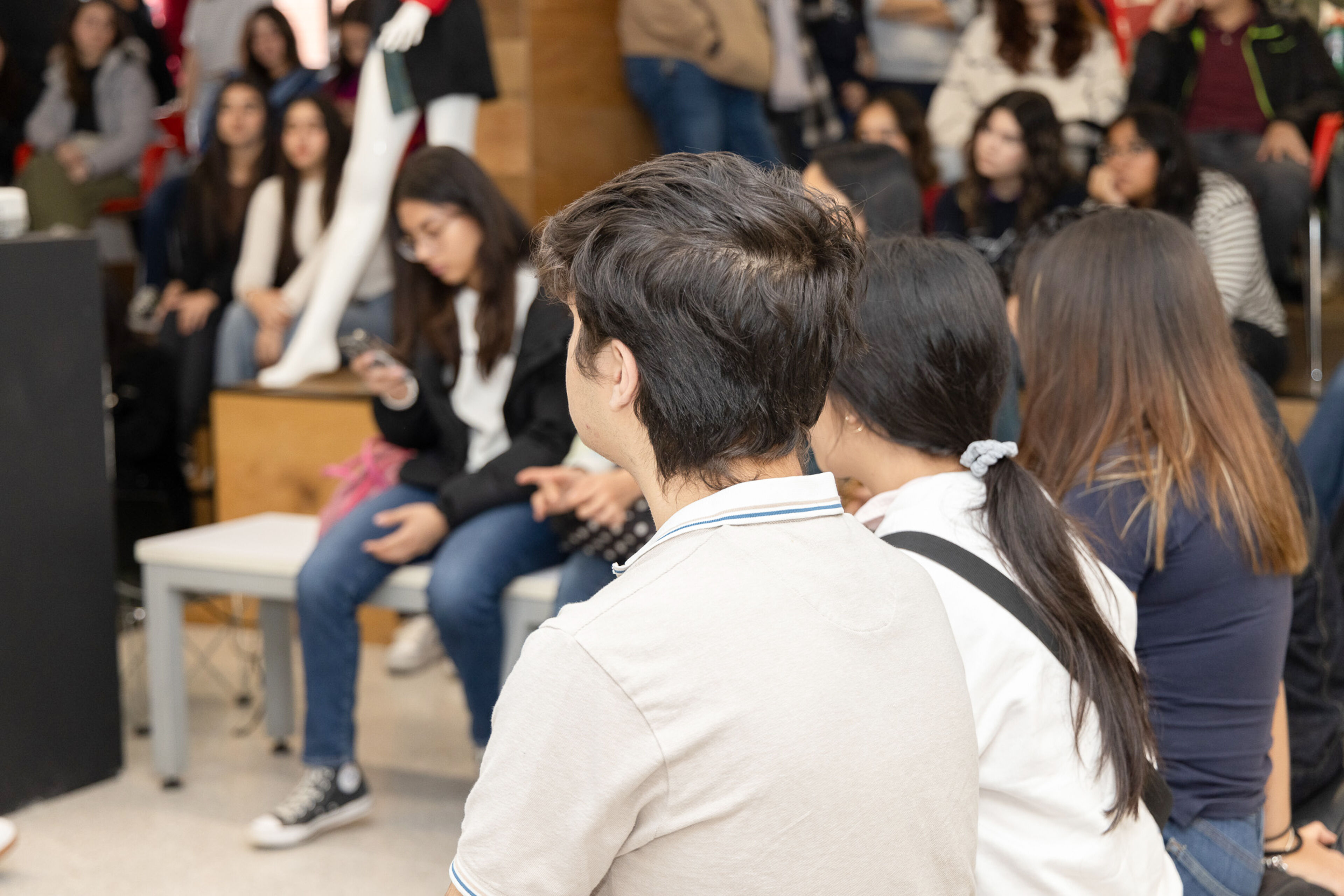 Adultos jóvenes escuchan atentamente en un evento público interior lleno de gente.
