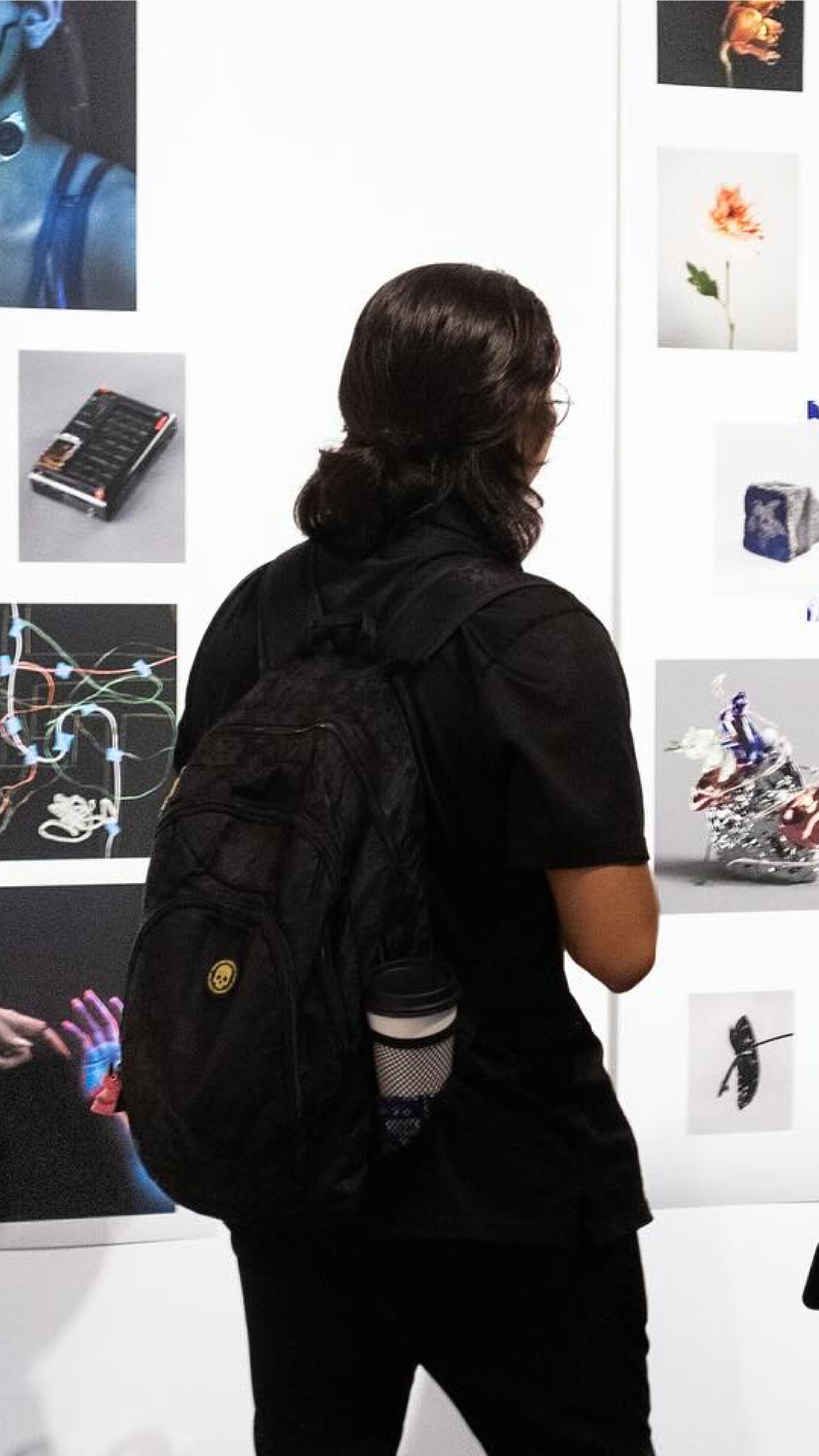 A person observing a wall of diverse photographs at a 2023 student photography exhibition.