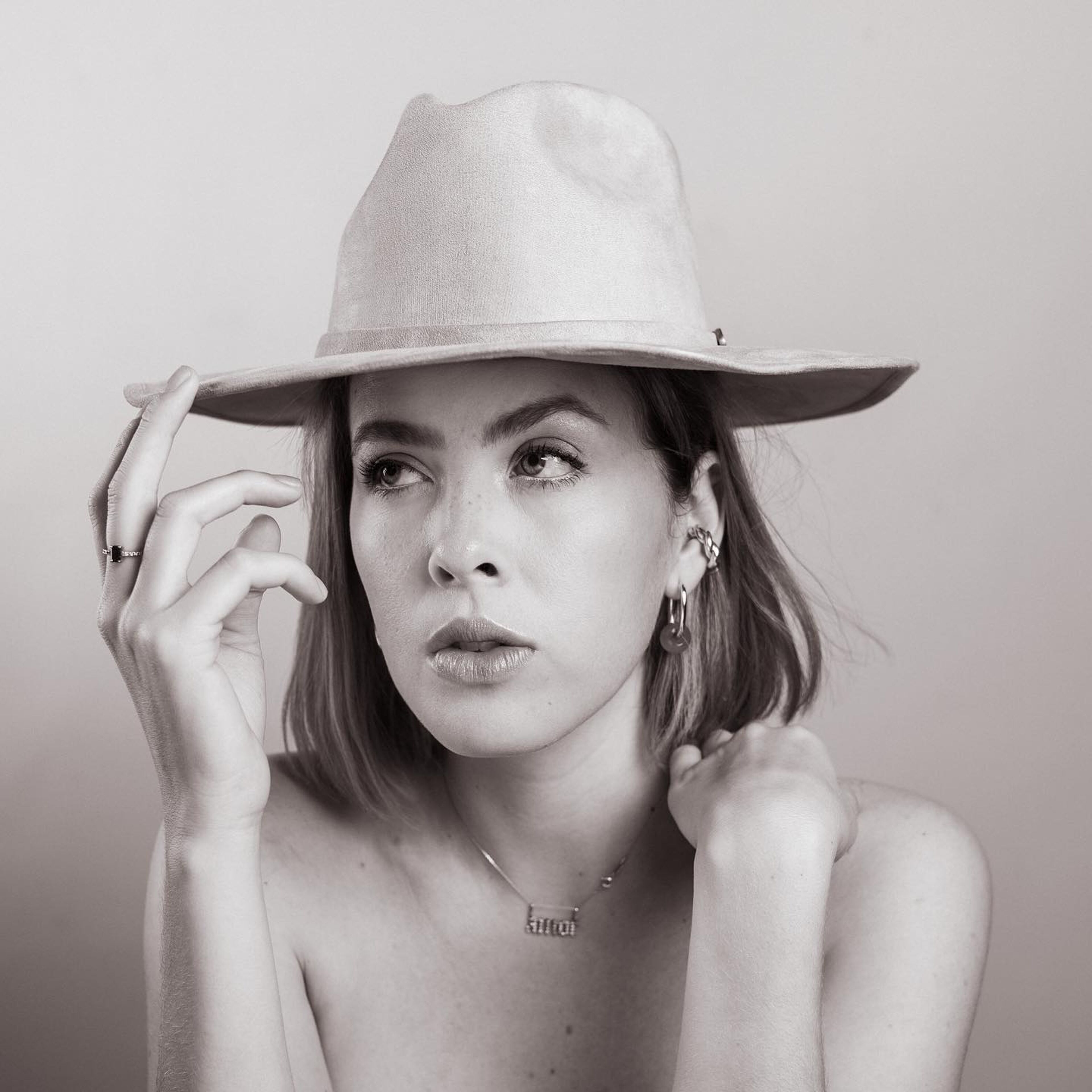 Retrato en blanco y negro de una mujer pensativa con sombrero fedora, mirada sutil hacia un lado.