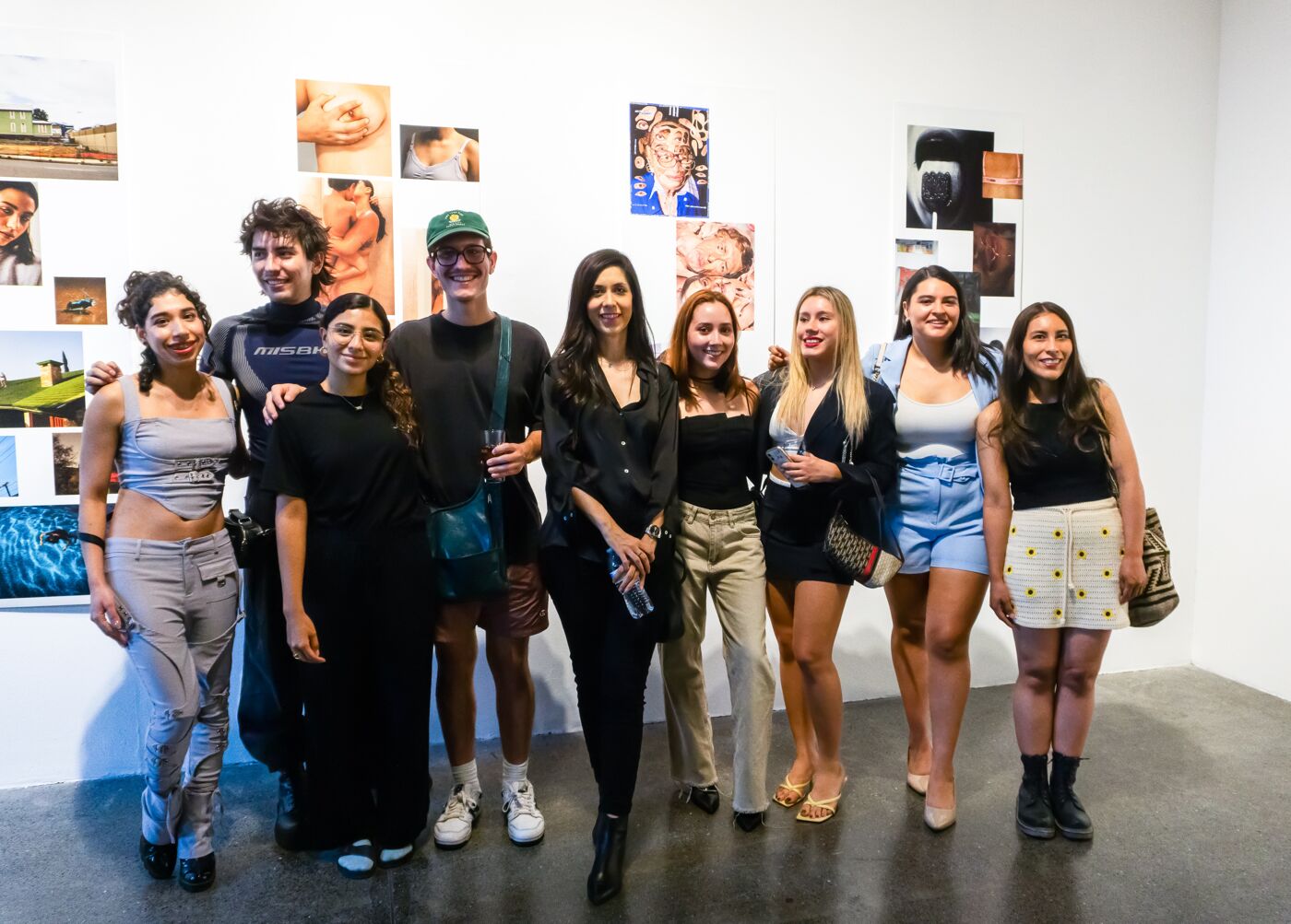 A group of eight smiling people posing in an art gallery, with various paintings in the background.