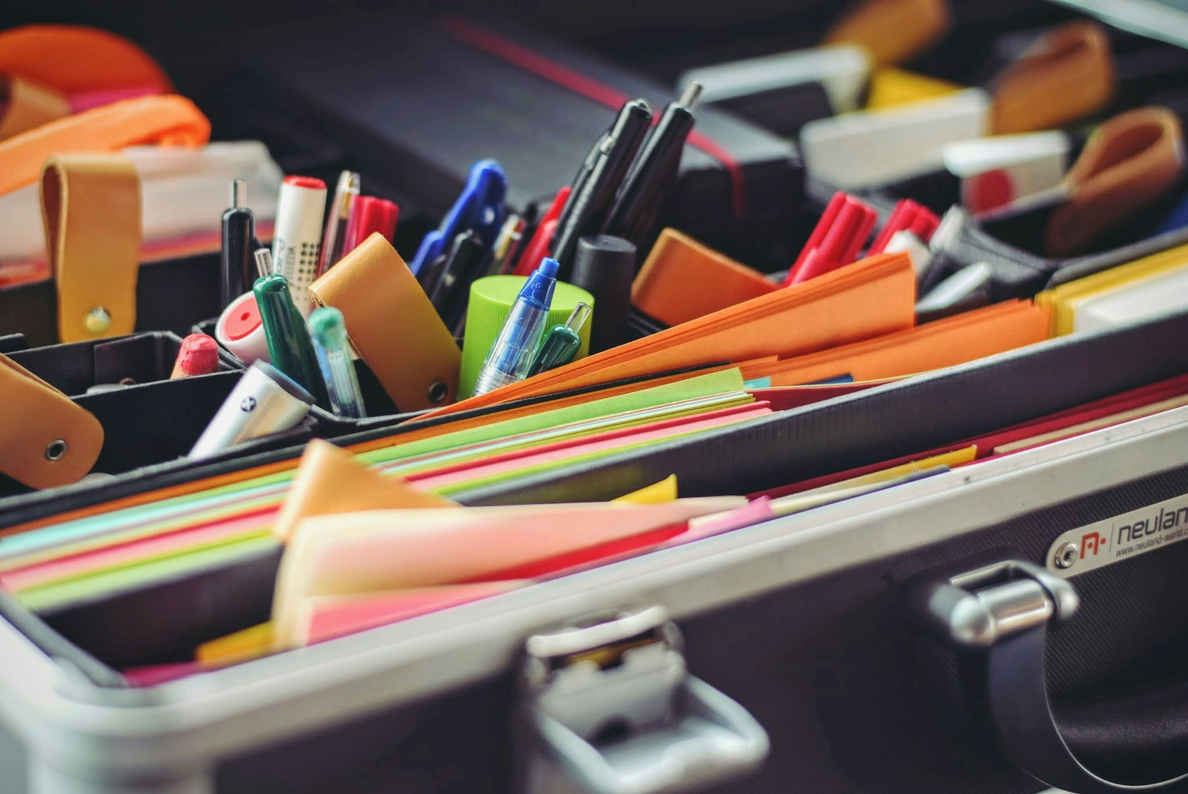 Variedad de artículos de papelería ordenados en un maletín portátil, incluyendo bolígrafos, marcadores y carpetas de colores.