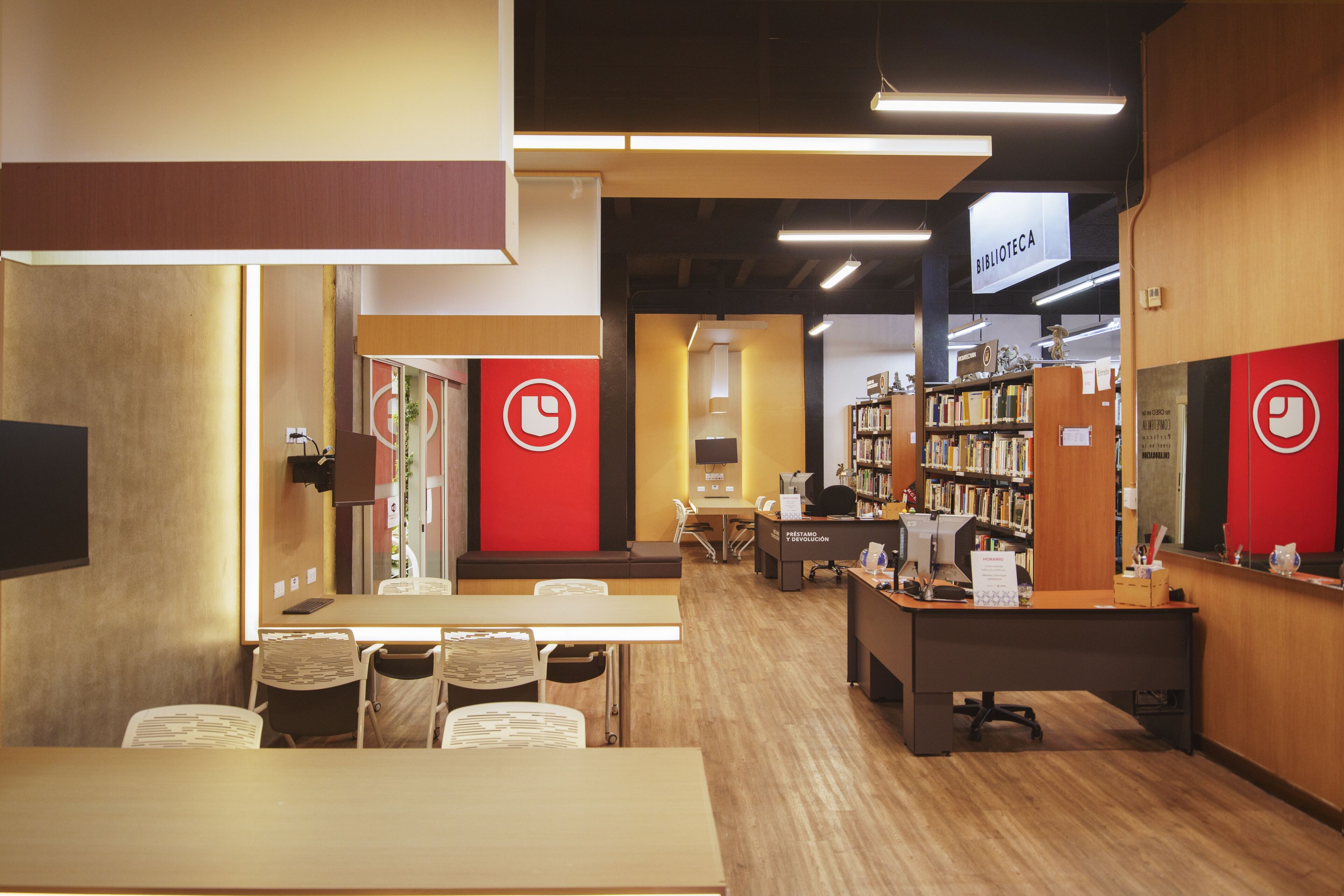 A contemporary library setting with organized bookshelves, study tables, and warm lighting, featuring a prominent red logo.