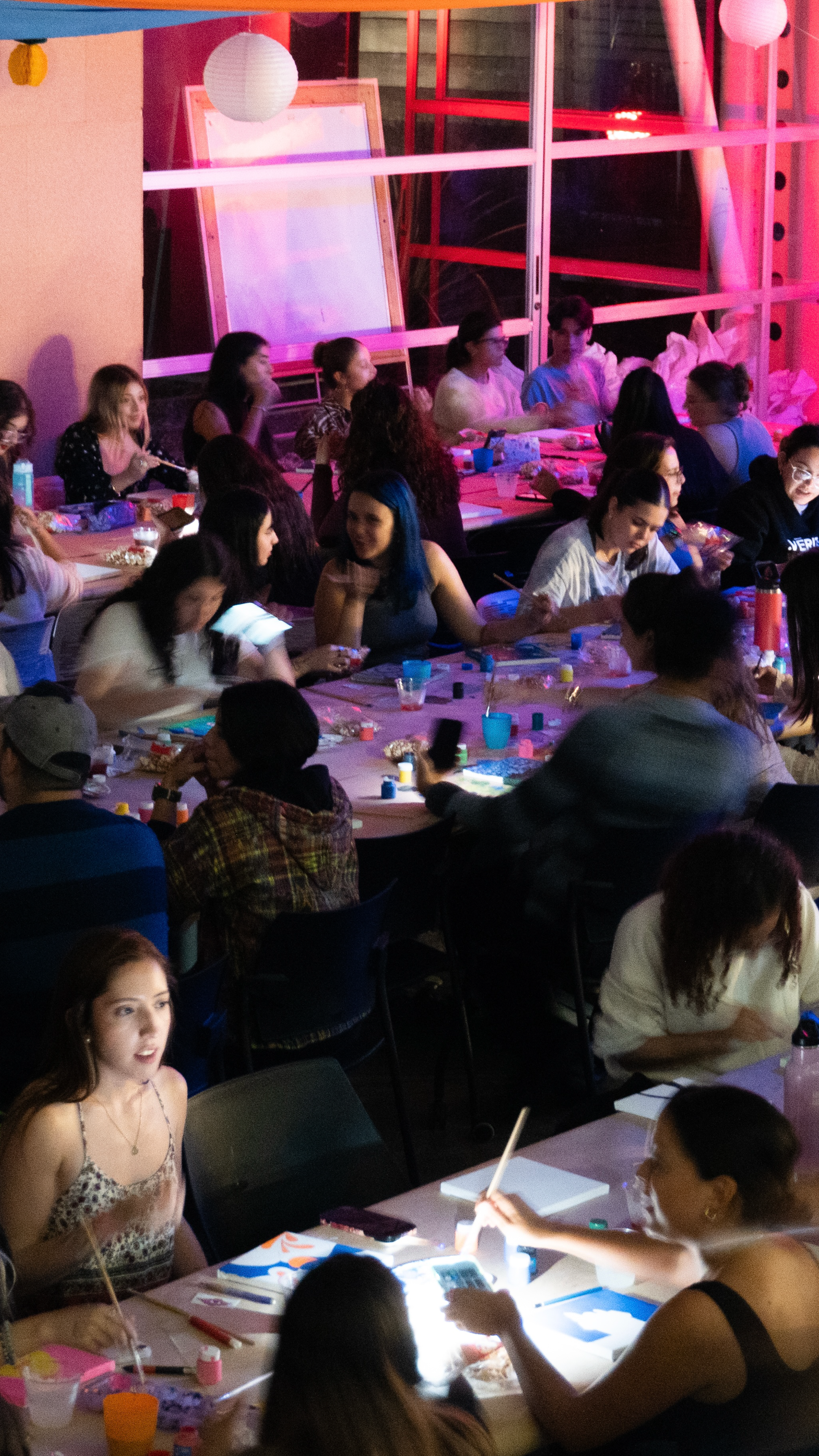 A bustling indoor art workshop, with participants focused on painting, illuminated by soft overhead lighting.