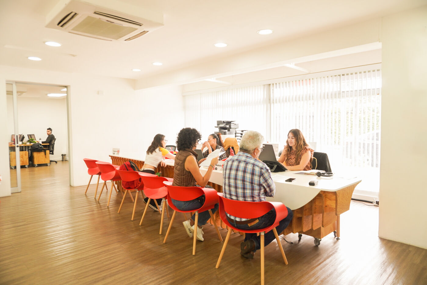 A group of professionals engaged in a discussion around a conference table in a brightly lit, contemporary office setting.

