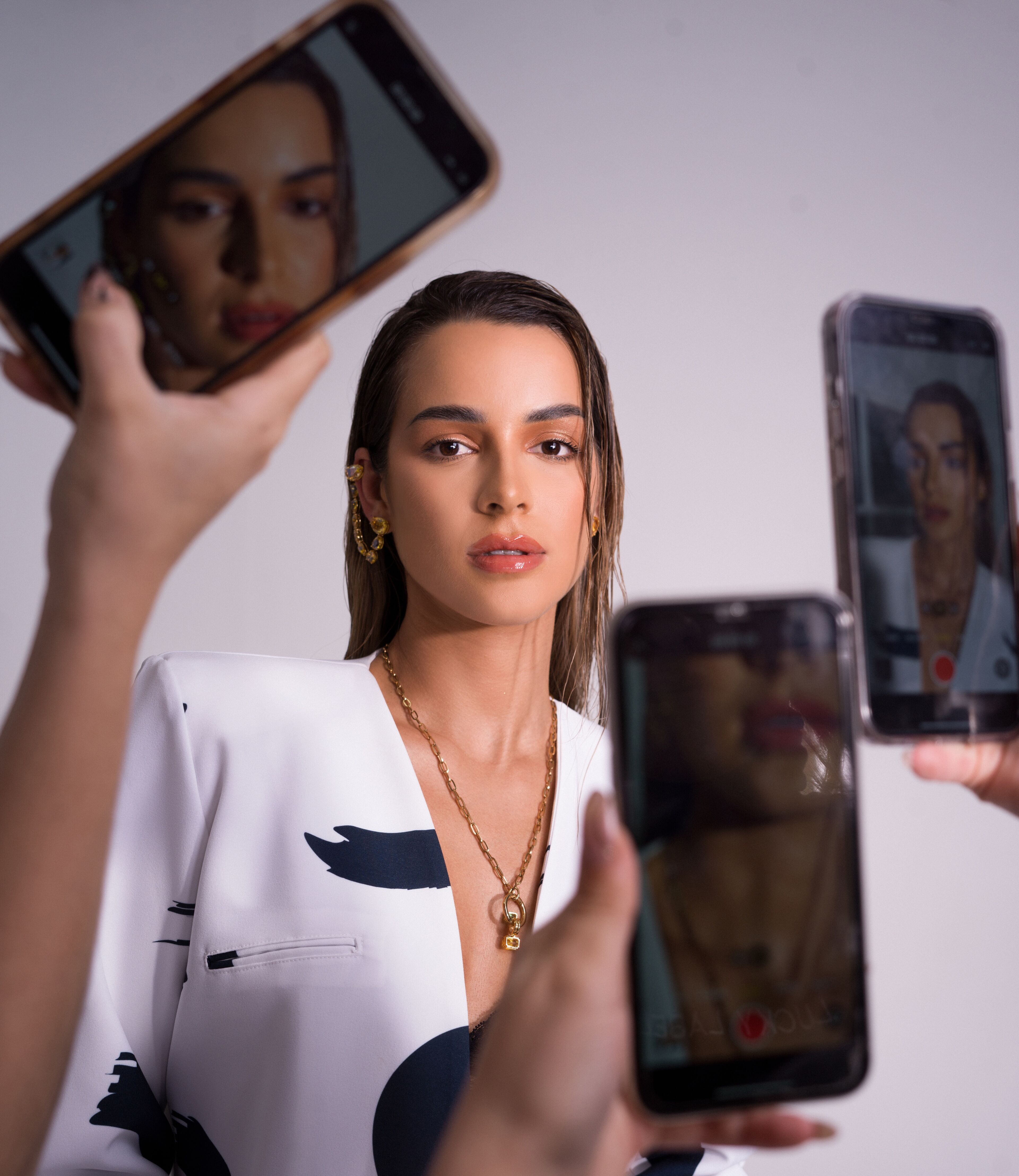 Una mujer posando para una sesión de fotos, vista a través de las cámaras de varios smartphones contra un fondo liso.