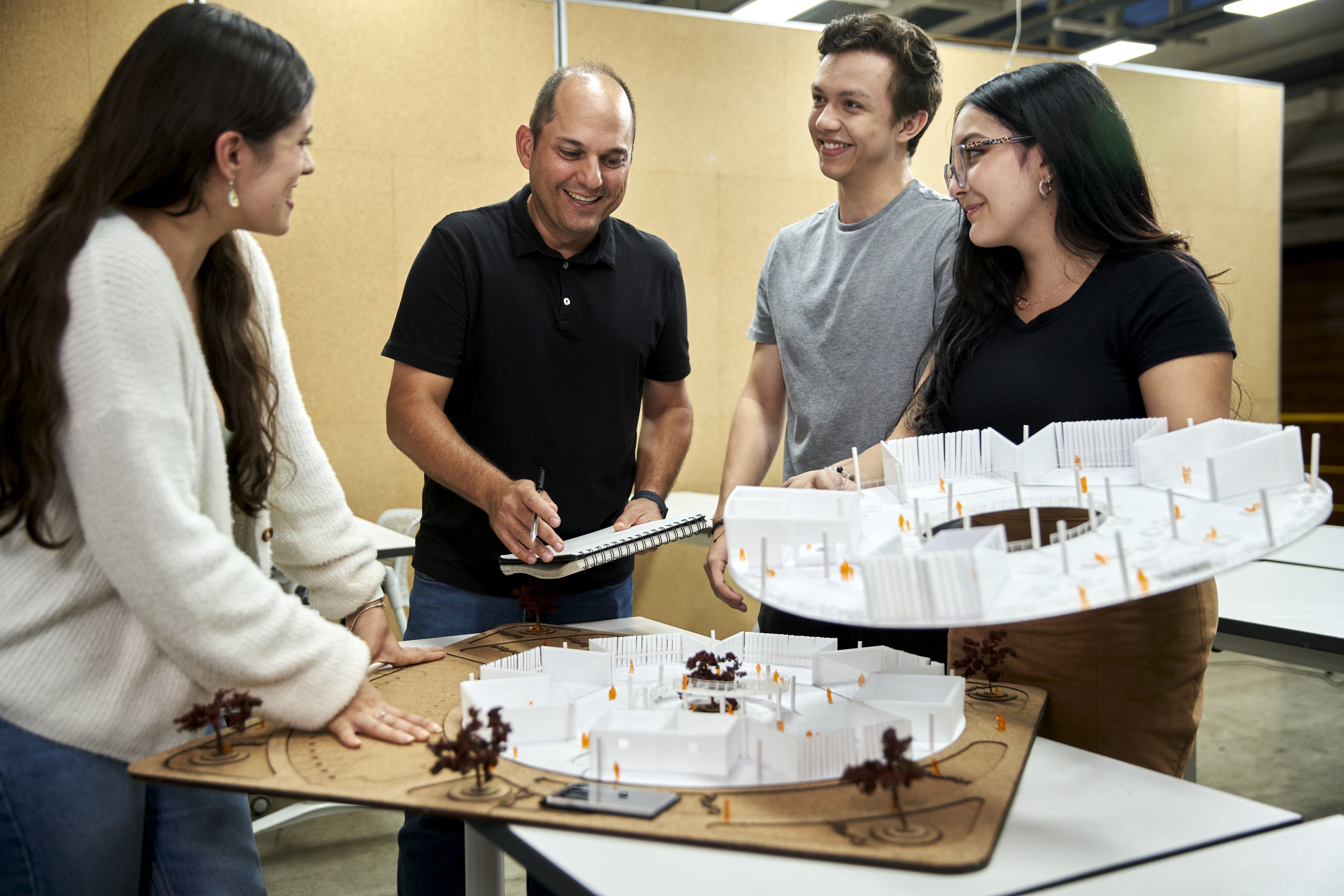 Cuatro profesionales se reúnen alrededor de un modelo arquitectónico detallado, discutiendo su diseño.