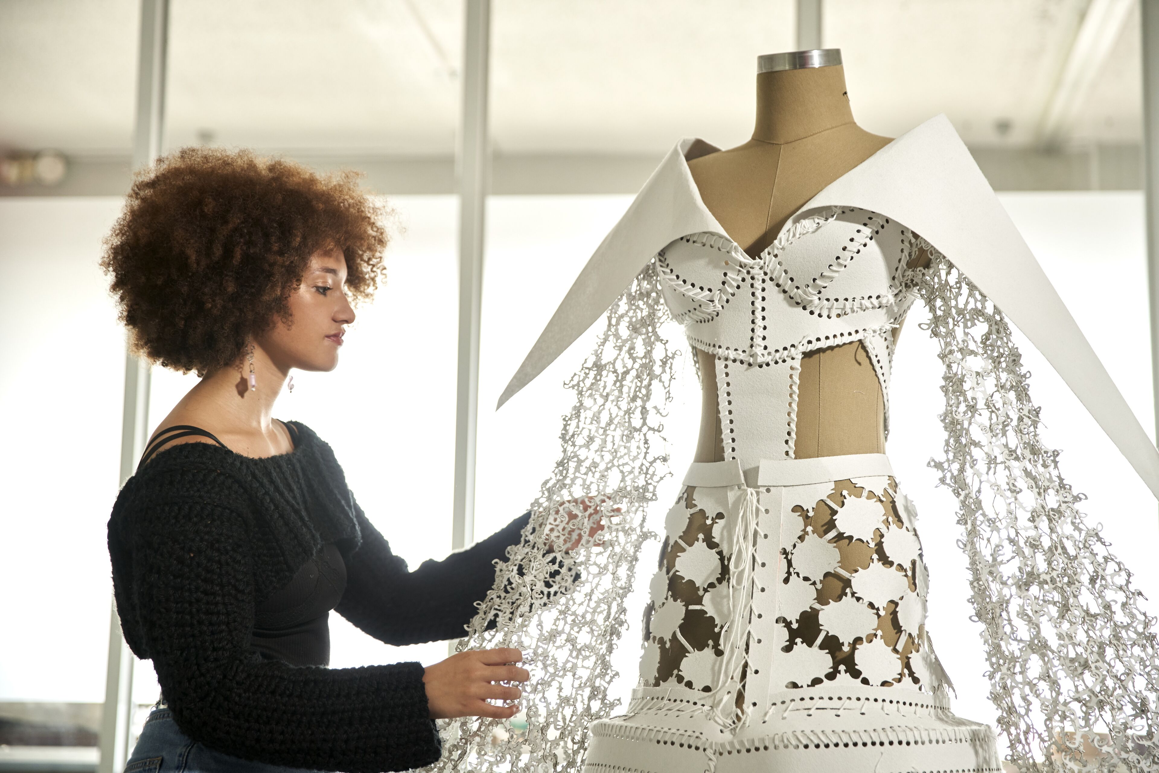 A fashion designer adjusts a lace detail on an avant-garde dress on a mannequin.