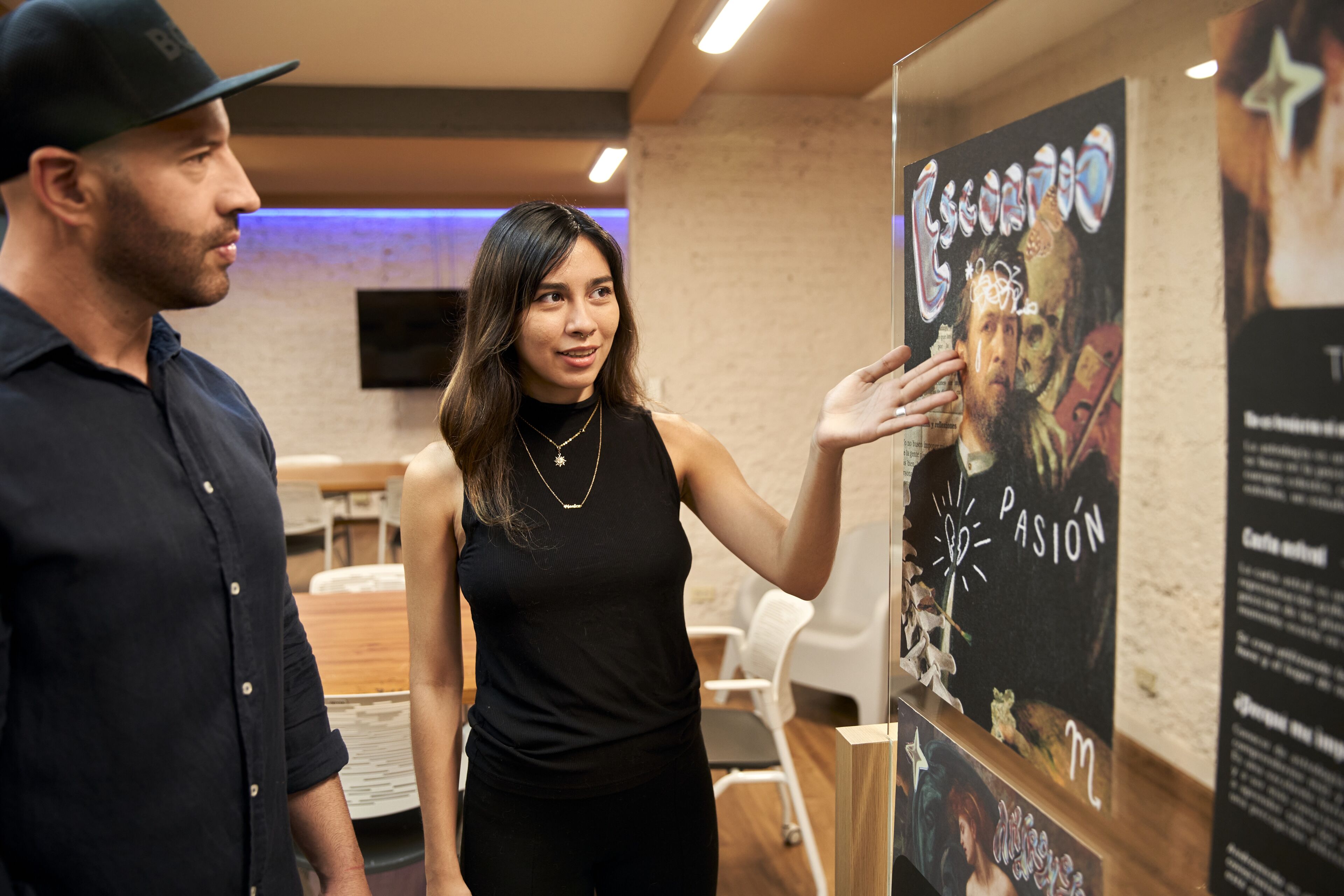 A woman in a black sleeveless top presents a chalkboard art piece to a man in a café setting.