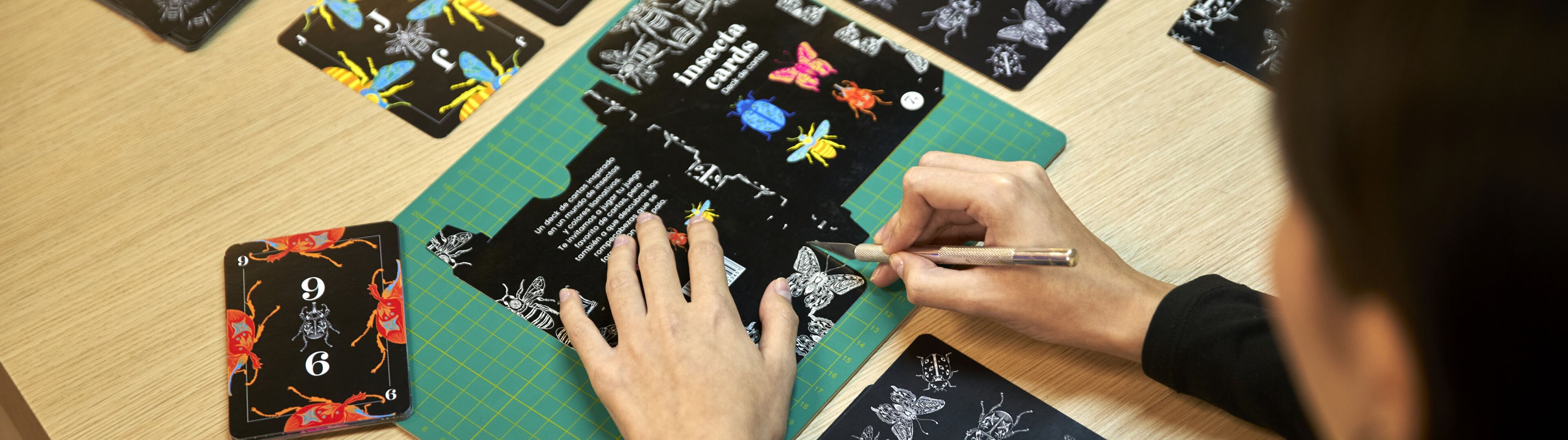 Una persona se dedica a elaborar intrincados diseños de cartas, enfocándose en una con motivos de mariposas coloridas.