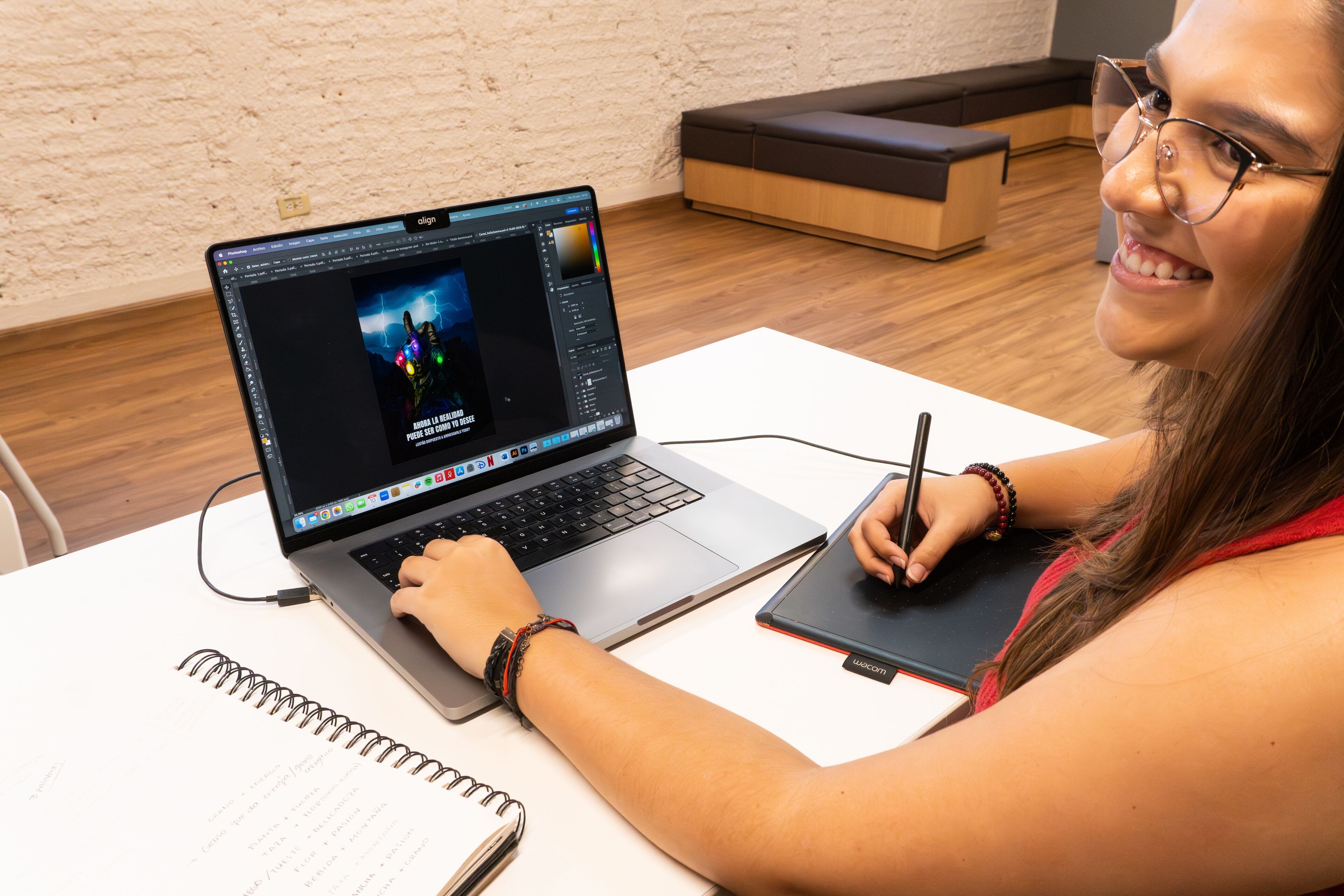 Una joven sonriente trabajando en diseño gráfico digital con una tableta gráfica y un lápiz óptico en su portátil.