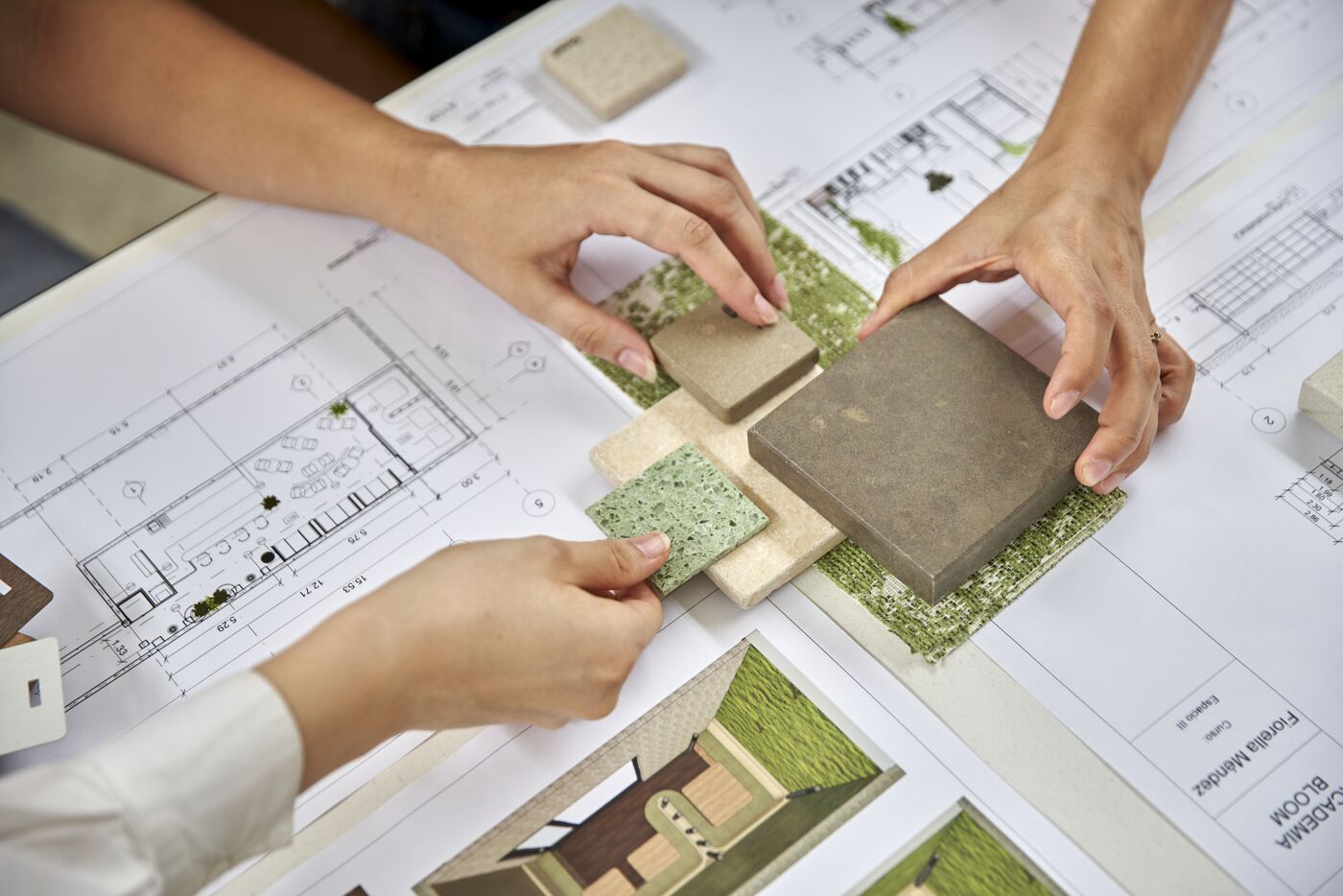 Two professionals comparing building materials over architectural blueprints and landscape plans.