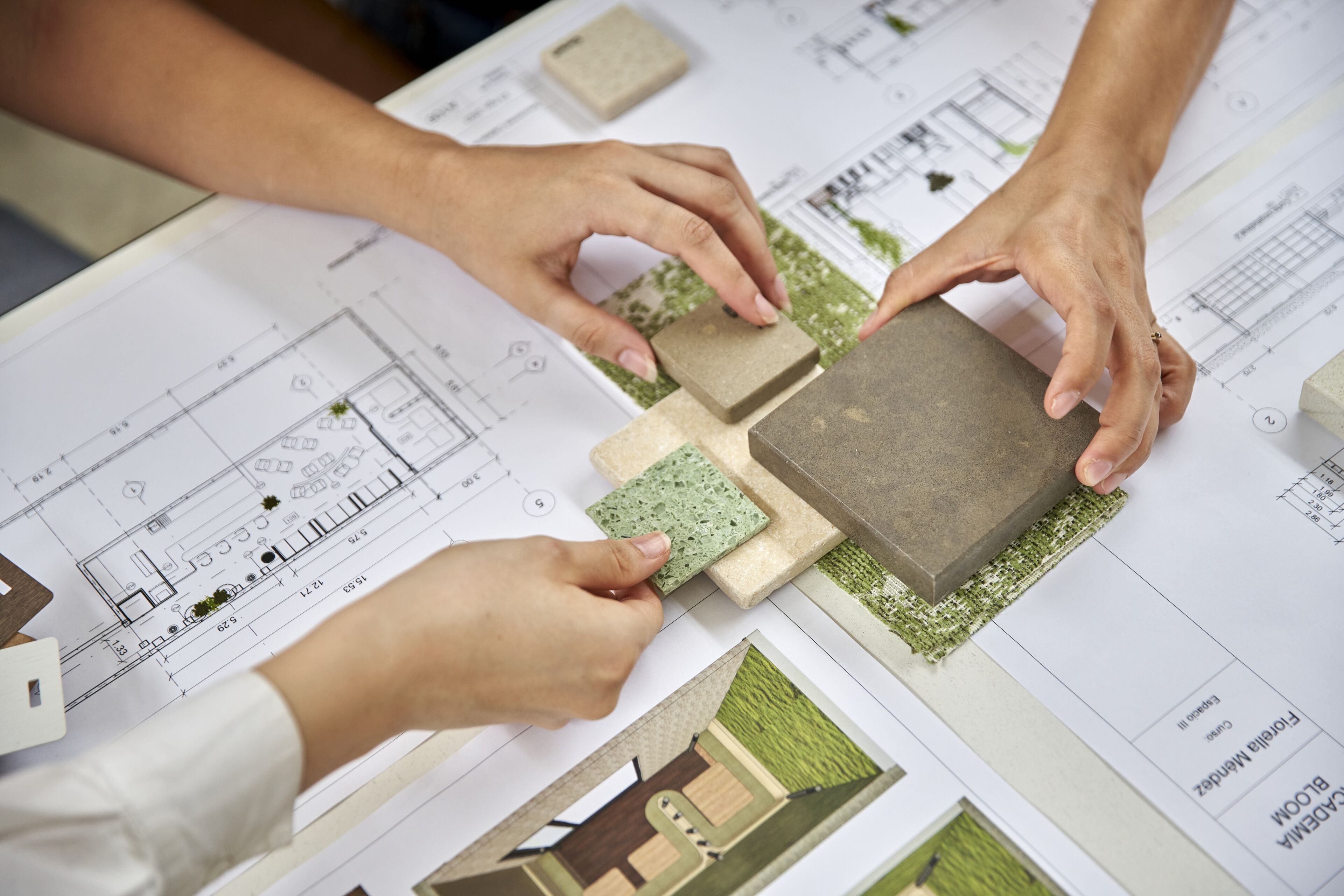 Dos profesionales comparan materiales de edificación sobre planos arquitectónicos y de paisajismo.
