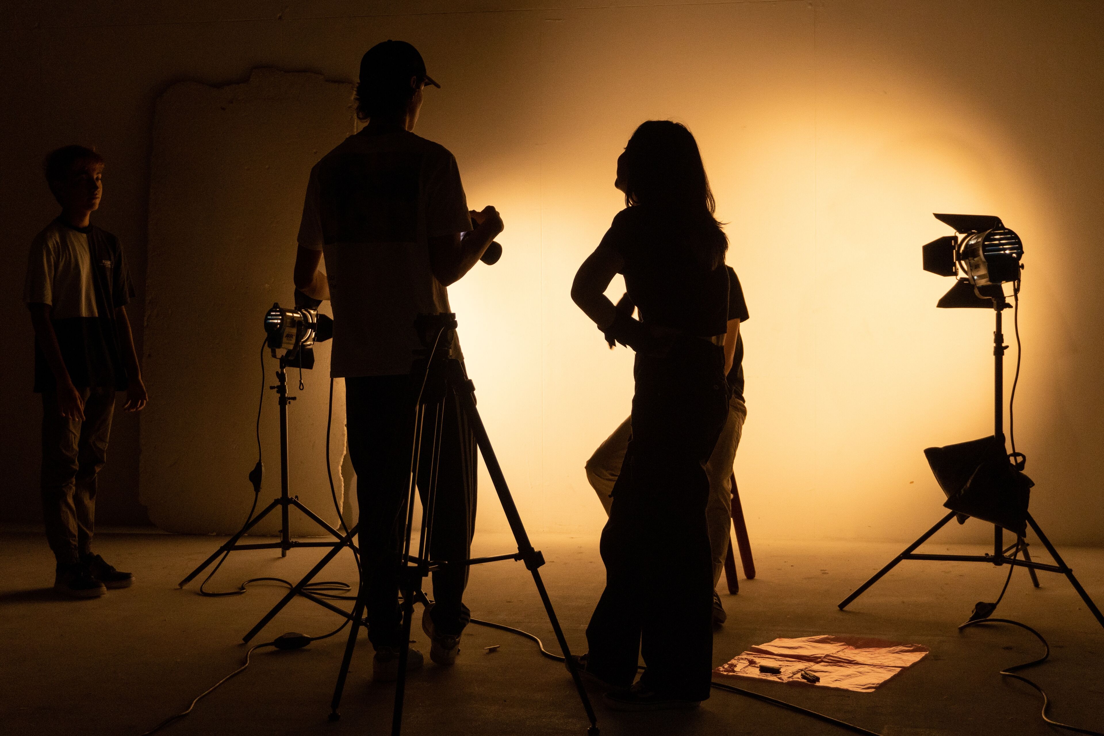 Siluetas de un equipo de filmación trabajando con equipos y luces en el set, capturando la actuación de un joven actor.