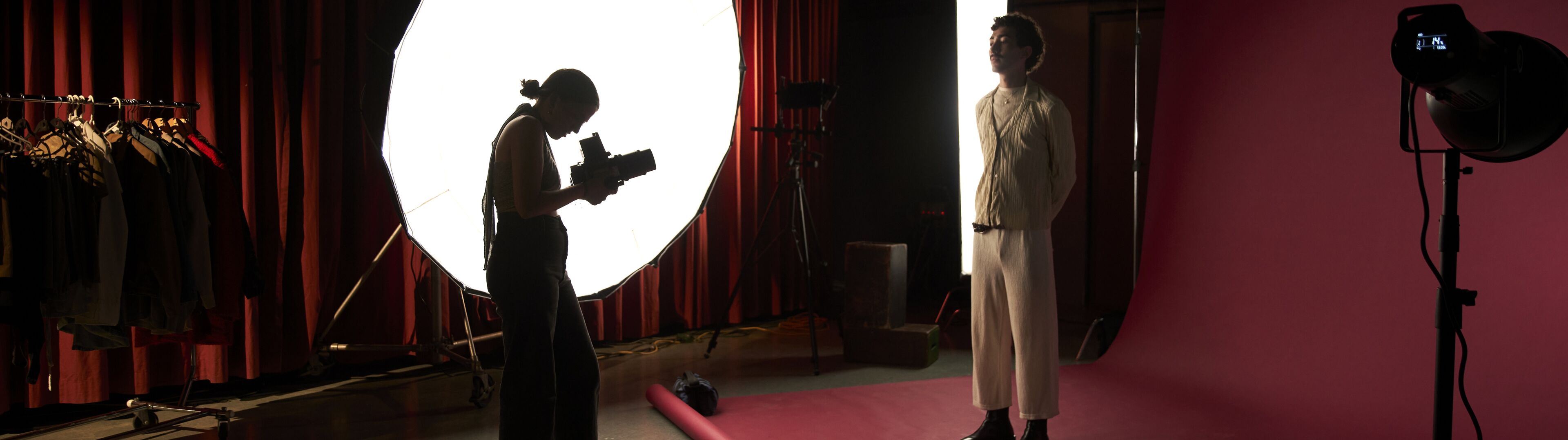 Un fotógrafo captura a un modelo en un ambiente de estudio estilizado, iluminado por un gran difusor circular con equipo de iluminación profesional.