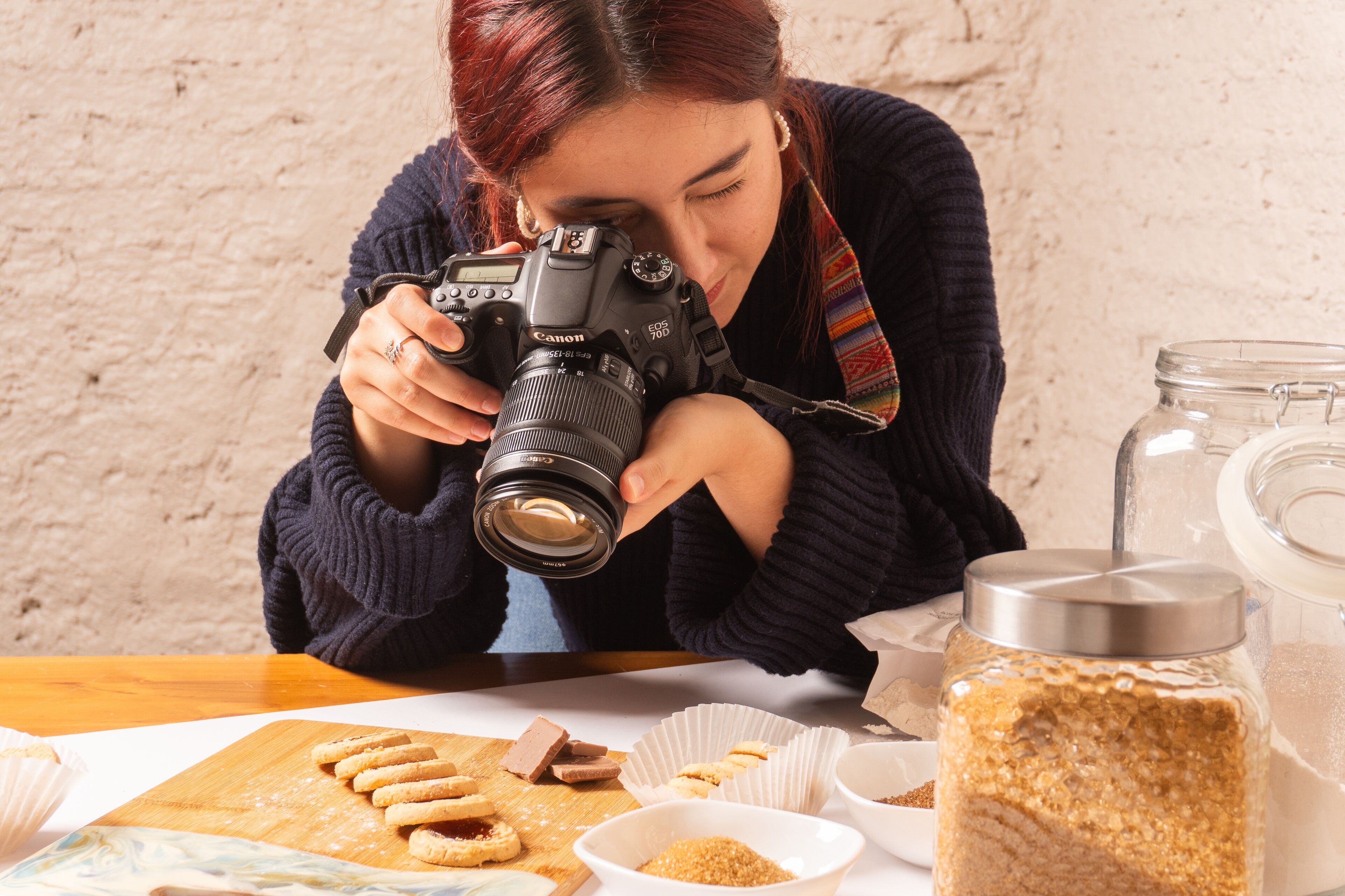 Fotógrafo(a) enfocado(a) toma primeros planos de galletas recién horneadas en una tabla de madera, rodeado(a) de ingredientes.