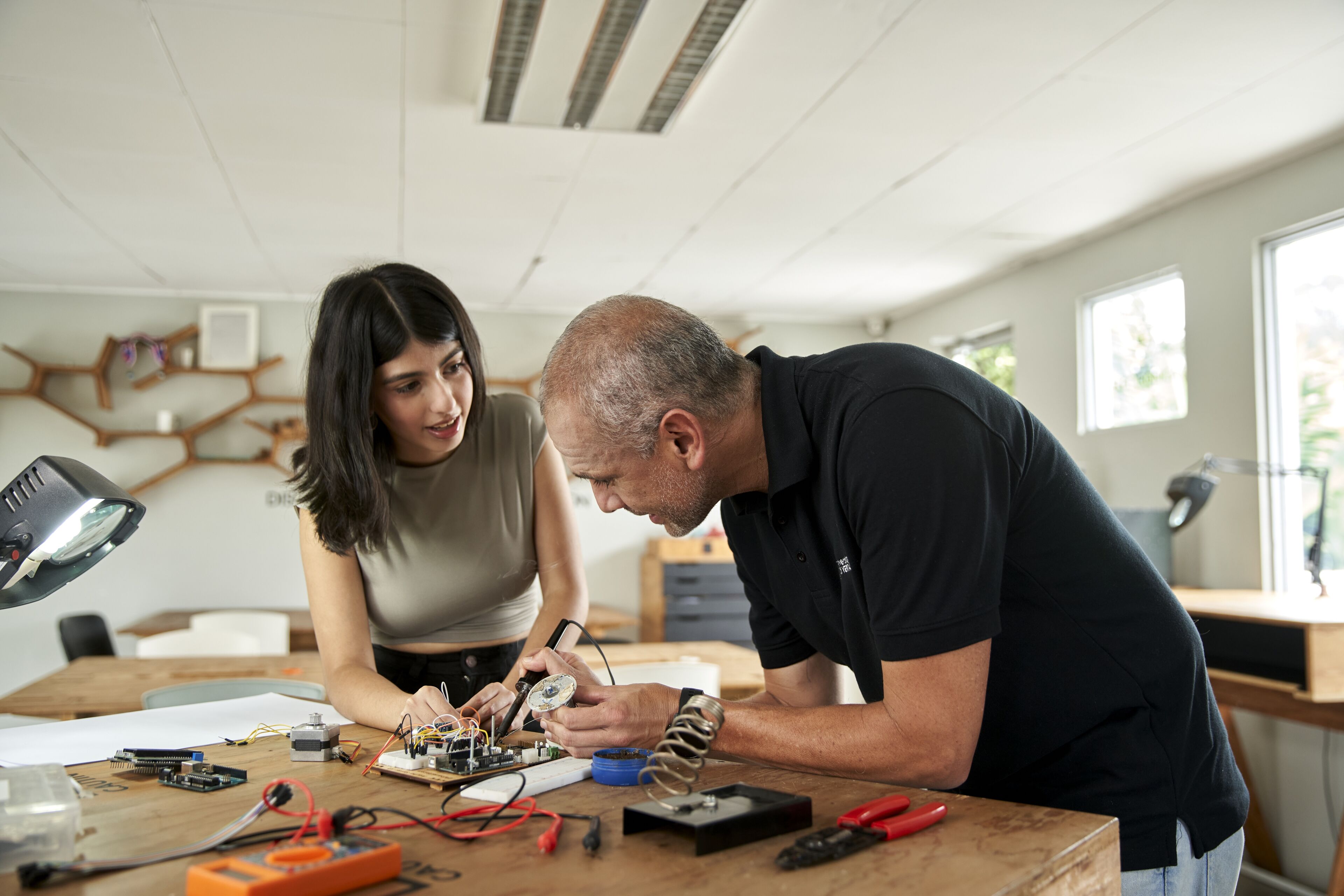 Un hombre y una mujer trabajan juntos en un proyecto electrónico en un taller iluminado.