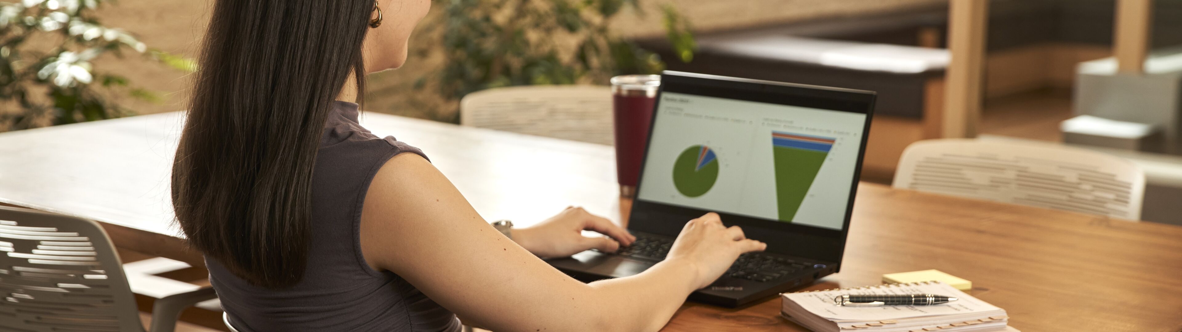 Una mujer profesional enfocada revisa gráficos circulares en un portátil en una oficina, con una bebida a su lado.