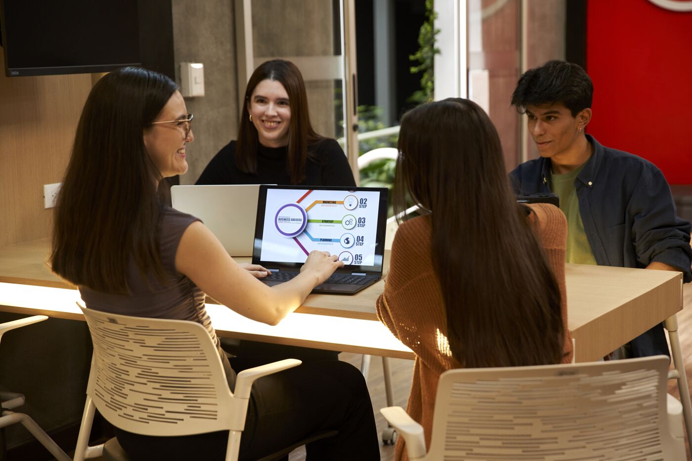 Four professionals engaged in a presentation, with one using a laptop to showcase a colorful diagram.