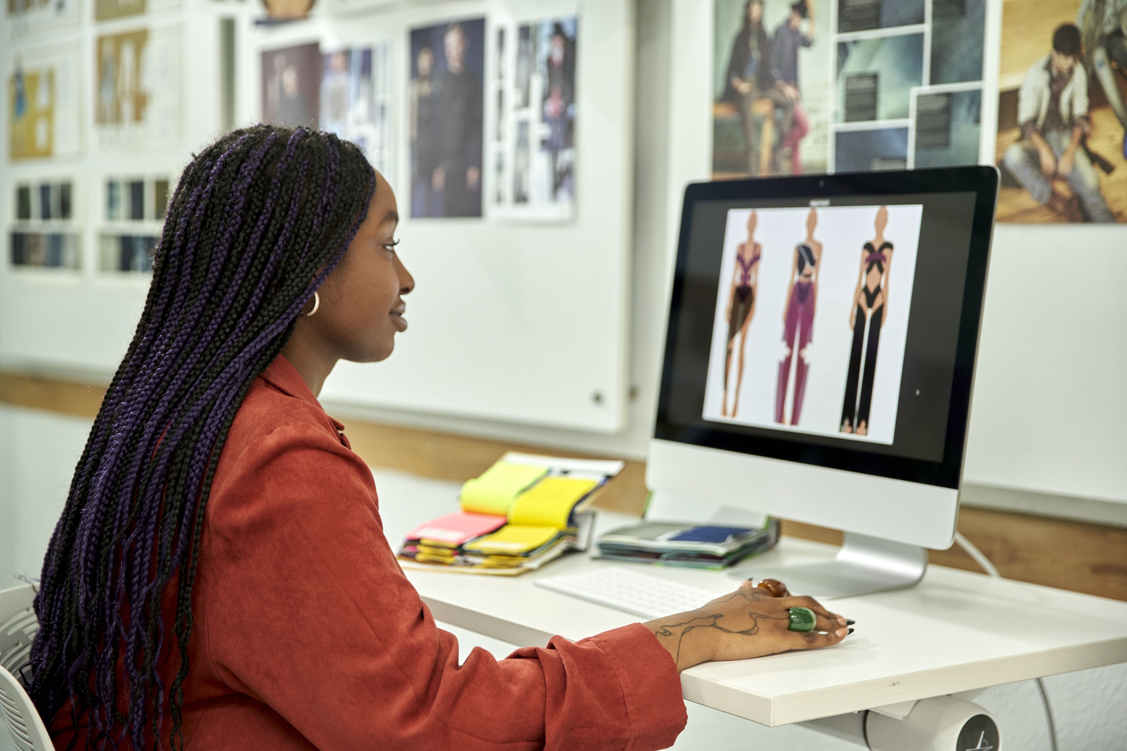 Una diseñadora de moda enfocada examina bocetos digitales de vestidos en su computadora en un estudio iluminado.