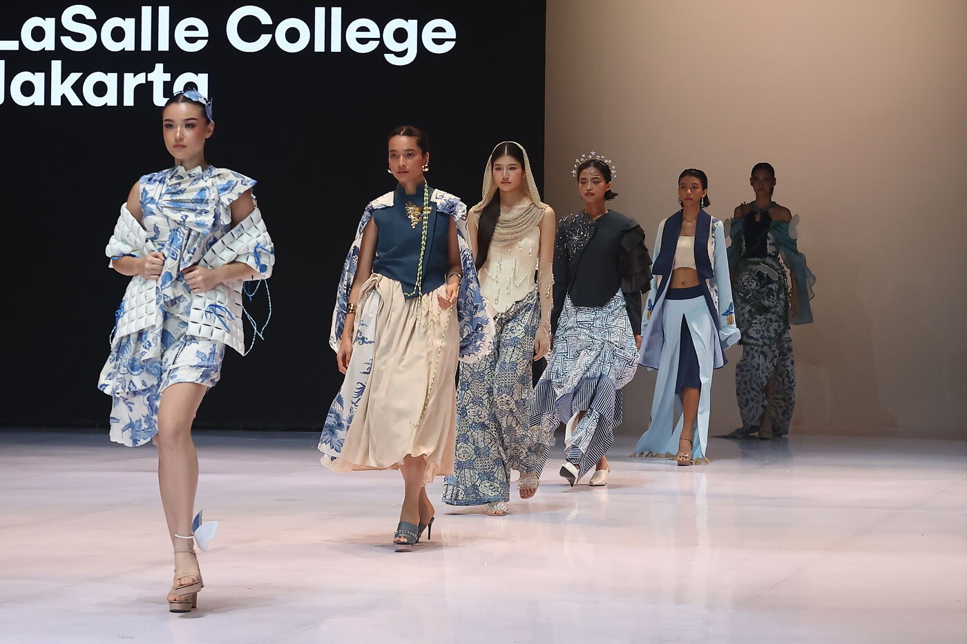 Models present fashion designs on a runway at La Salle College Jakarta, showcasing diverse styles and patterns.