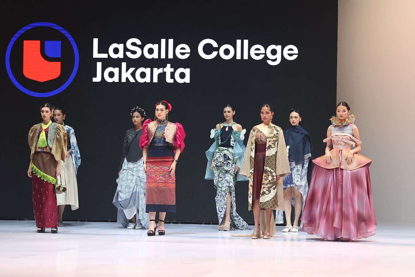 A fashion show at La Salle College Jakarta features diverse designs with models showcasing unique garments on a brightly lit runway.