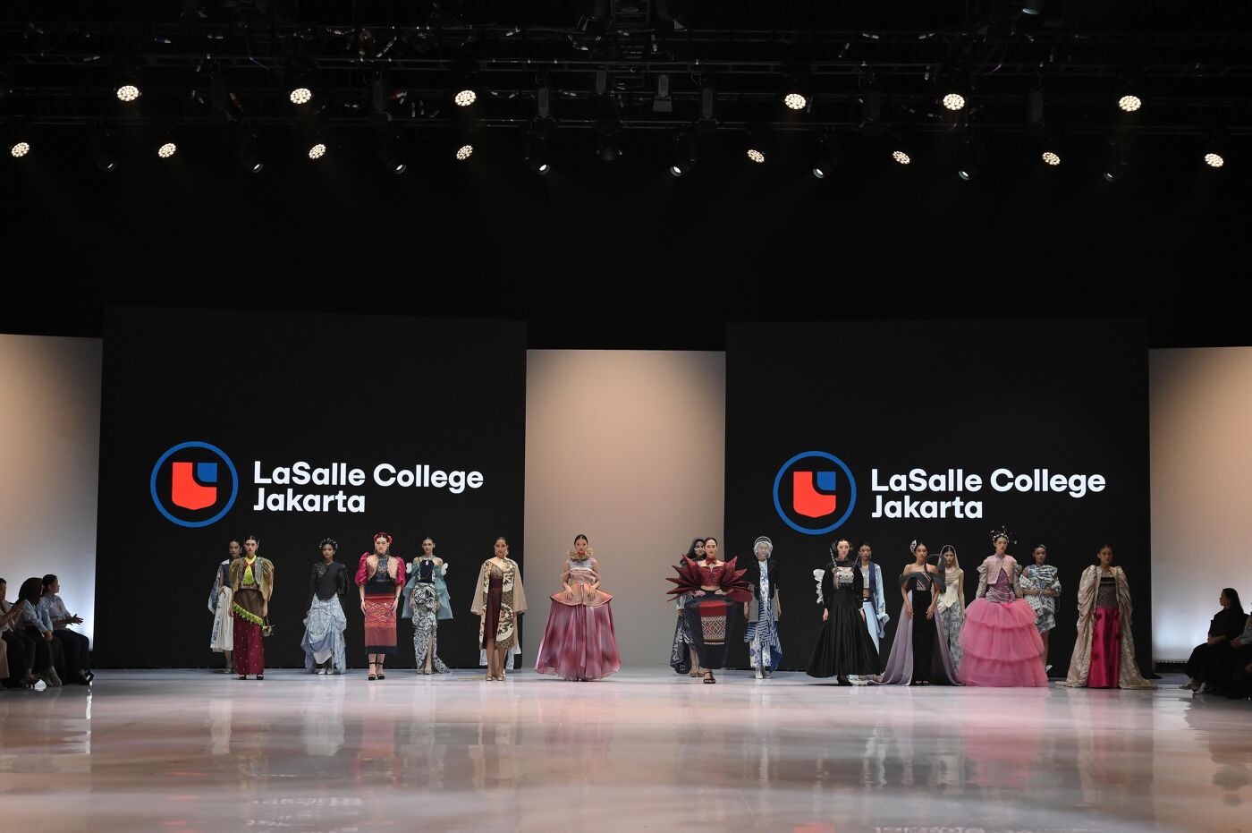 A group of people are modeling elegant outfits on a runway in front of the LaSalle College Jakarta logo.