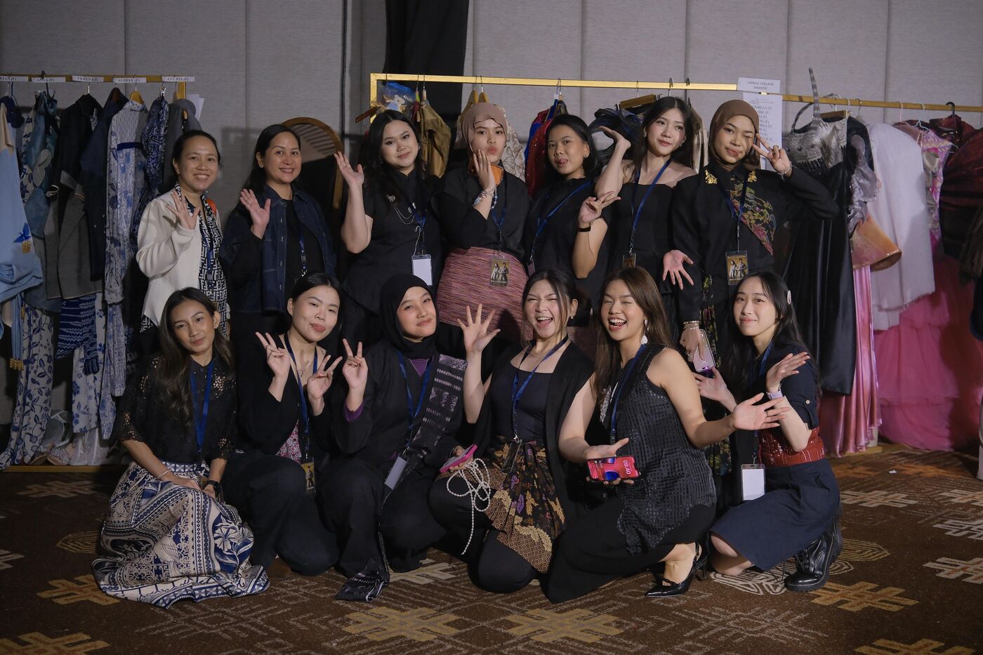 A group of young women pose for a group photo, some making peace signs, with traditional and modern outfits behind them.