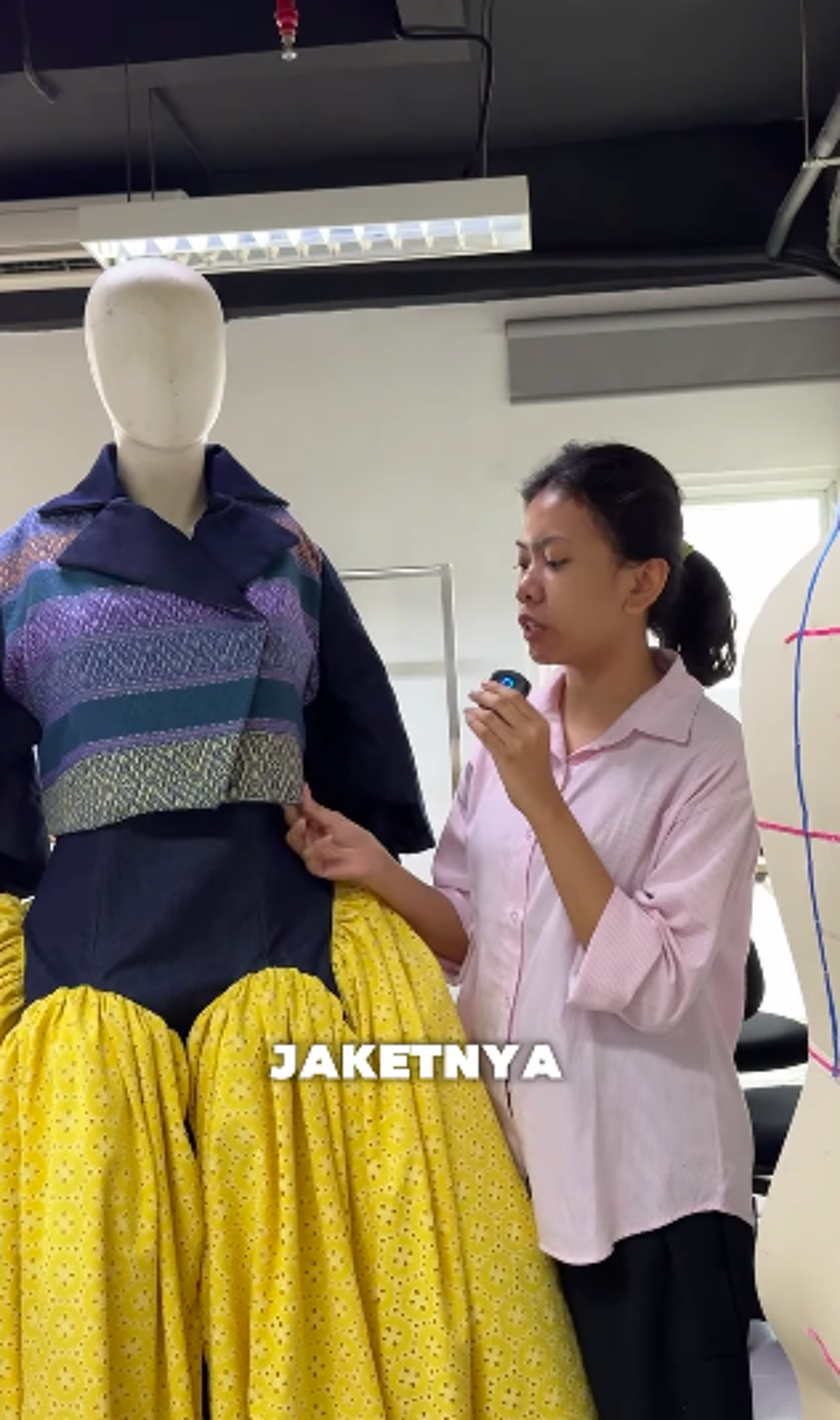A woman in a pink shirt examines a yellow and blue dress on a mannequin.