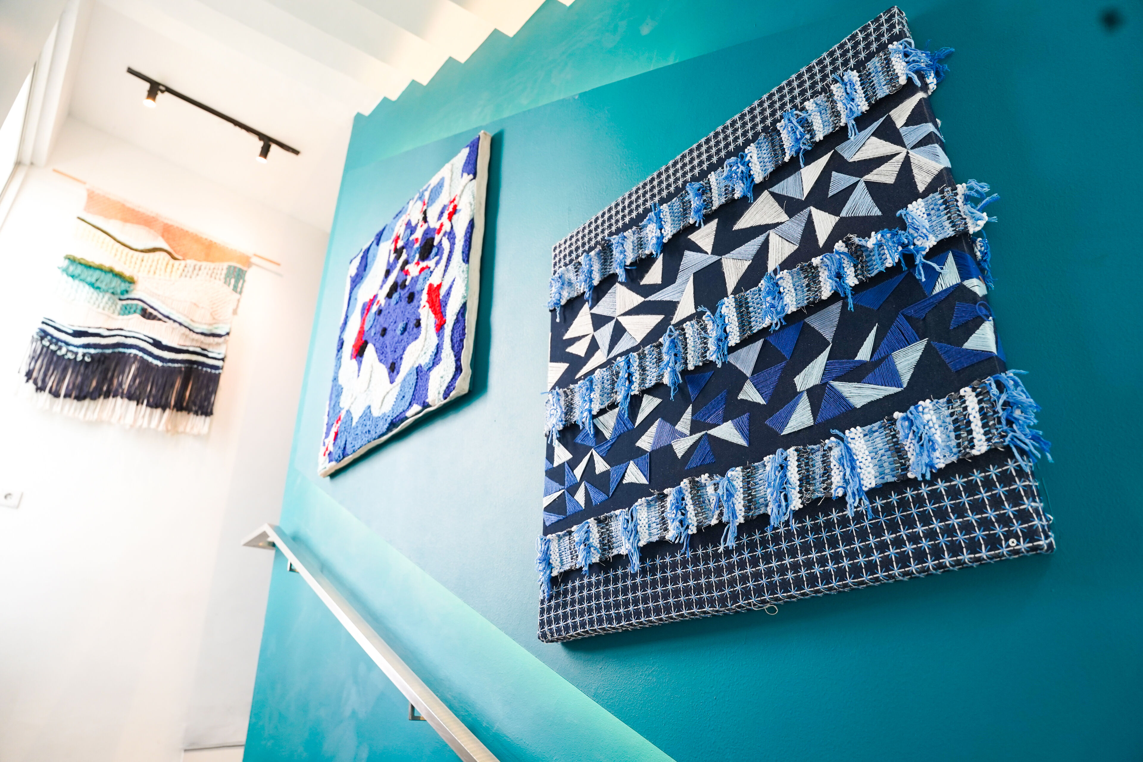 An interior wall featuring two unique pieces of textile art, one with abstract geometric patterns and another with varied textures and fringes, both adding a modern touch to the decor.